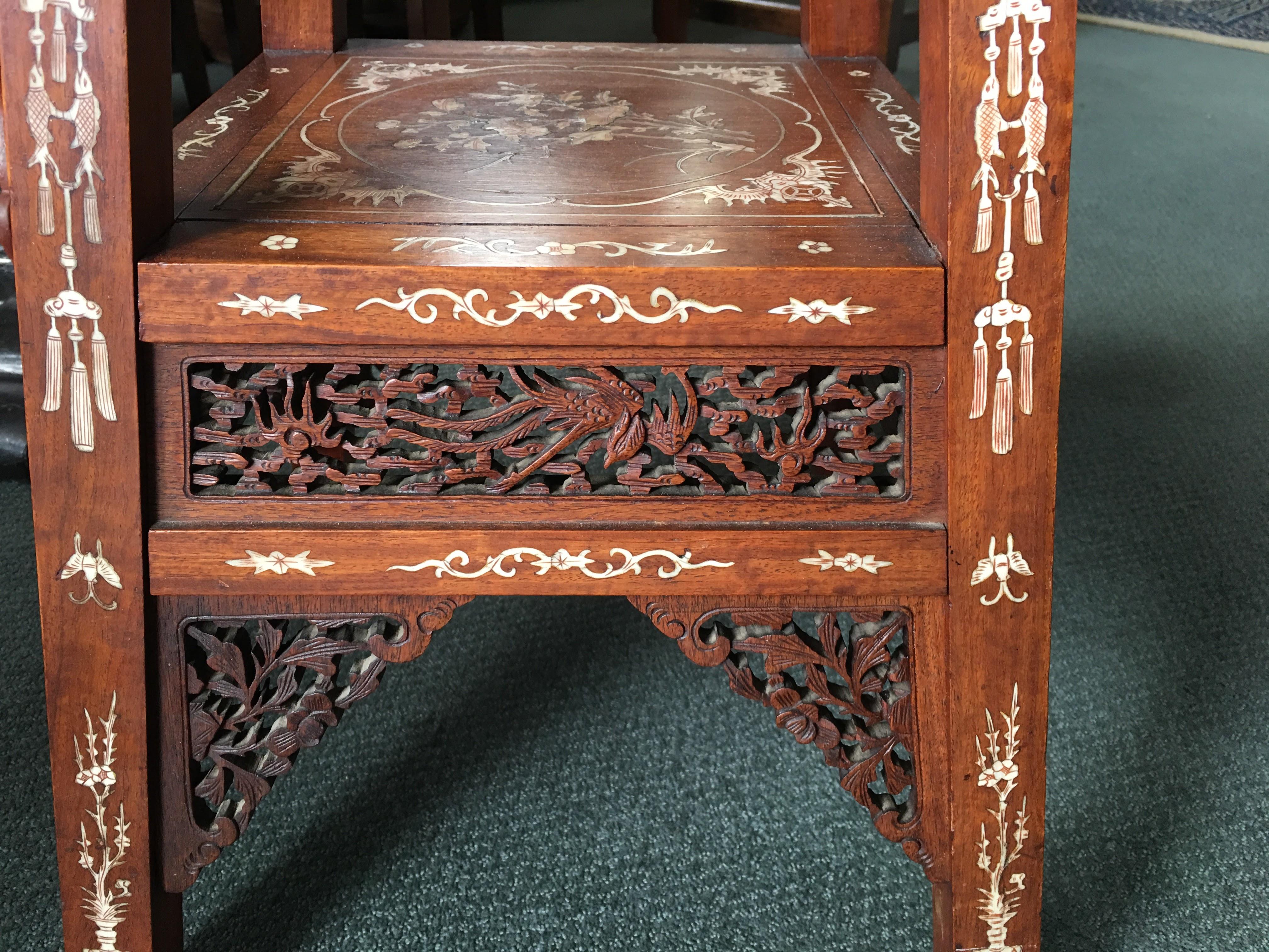 Chinese hardwood table of tapering square form, the legs and shelves with fine inlaid bone scenes including figures and pagodas, the skirt and brackets with finely carved openwork panels. Old paper label beneath with name and address, date 1931,