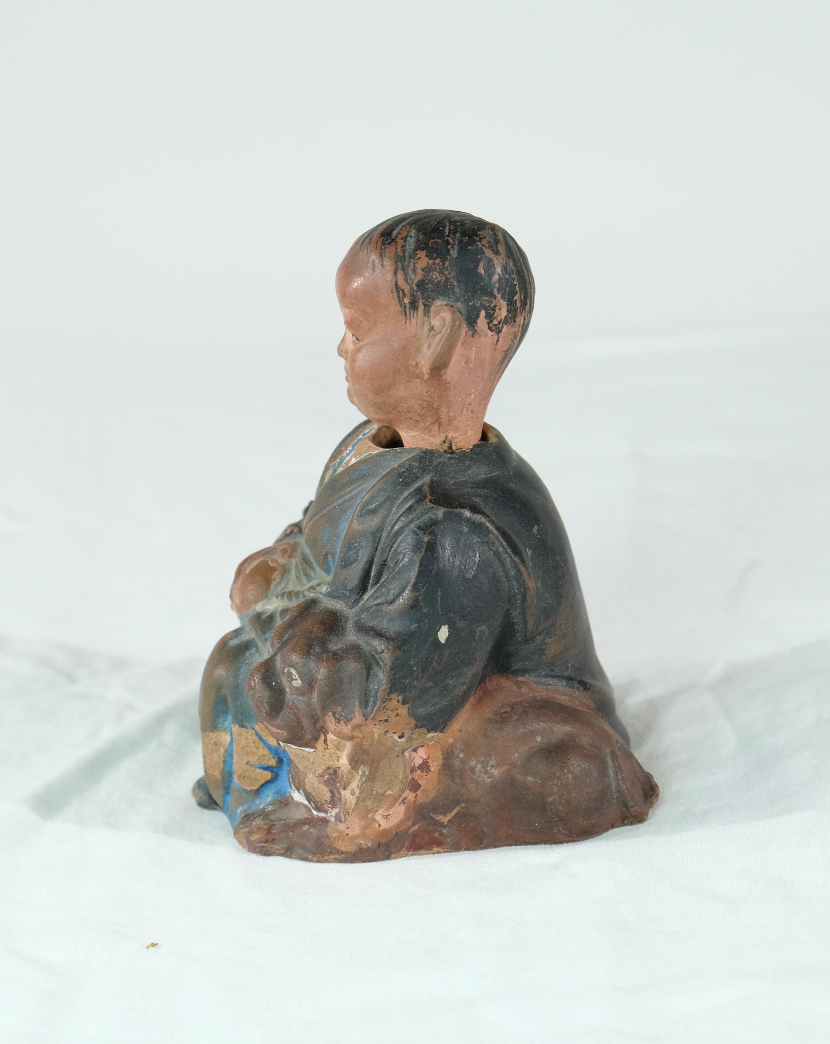 A charming head doll made of painted clay depicting a young boy. Below the doll is a note in Swedish that it was given as cristmas-present in 1925.