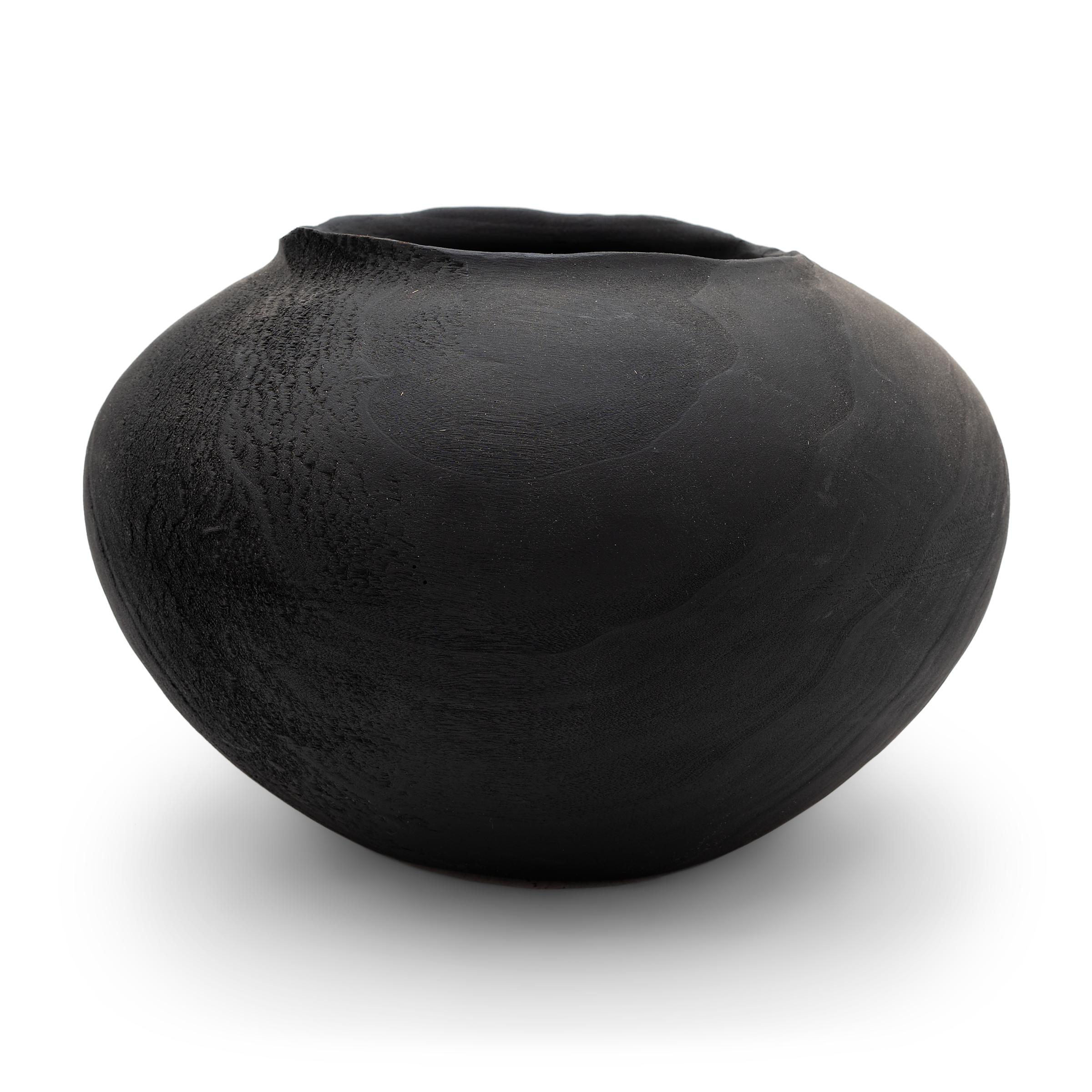This wooden bowl was turned from a solid block of heartwood, the dense, innermost portion of a tree. The vessel has a rounded body, shaped with a tapered base, shallow interior and slightly flared lip. The bowl has been stained dark for a matte
