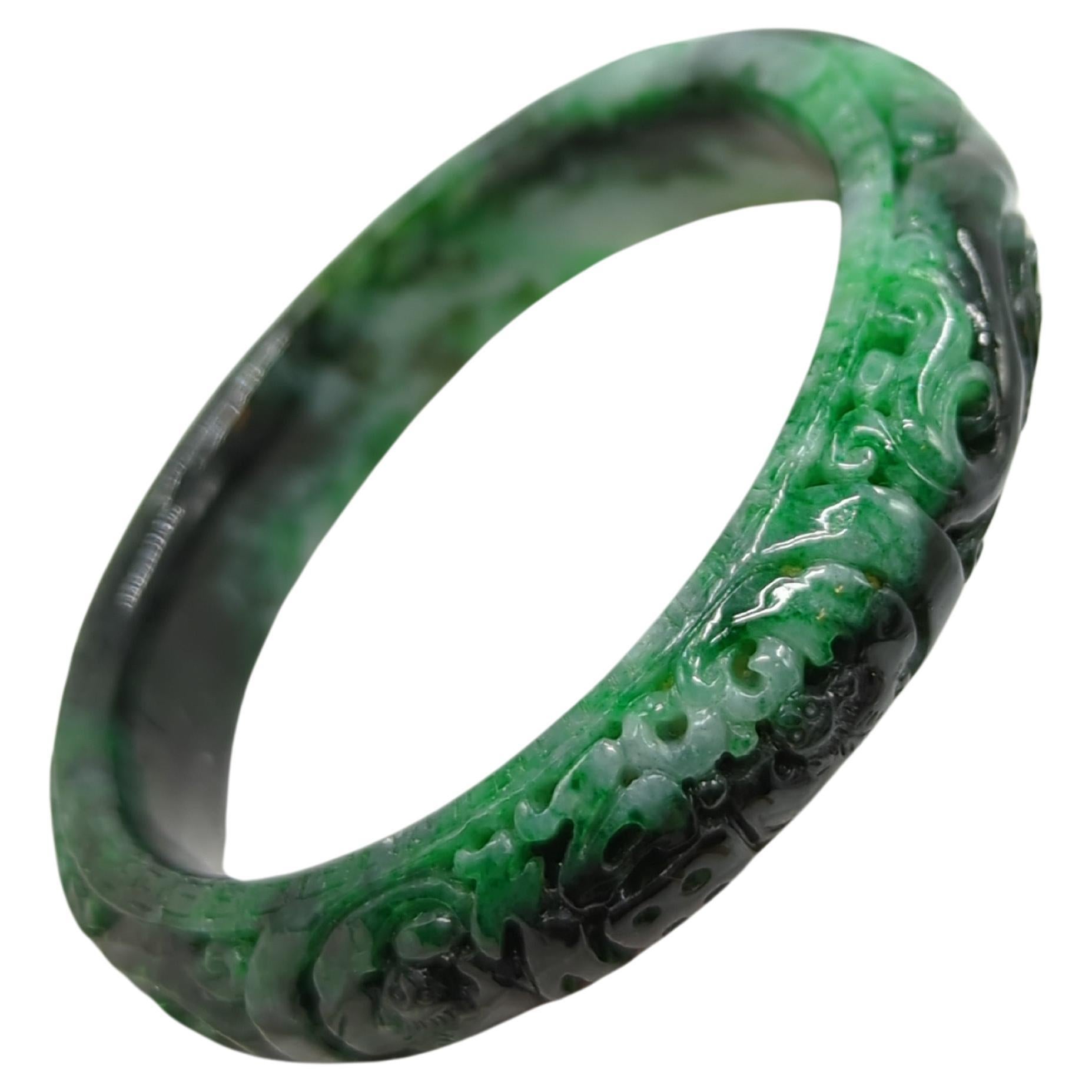 A heavily carved vintage Chinese natural jadeite bangle, with rich natural mottled colors including pale green, emerald green to dark ink green

ID: 60mm
OD: 79mm
Width: 14.5mm
Weight: 68 grams
Grade: A-grade jadeite, no enhancements, completely