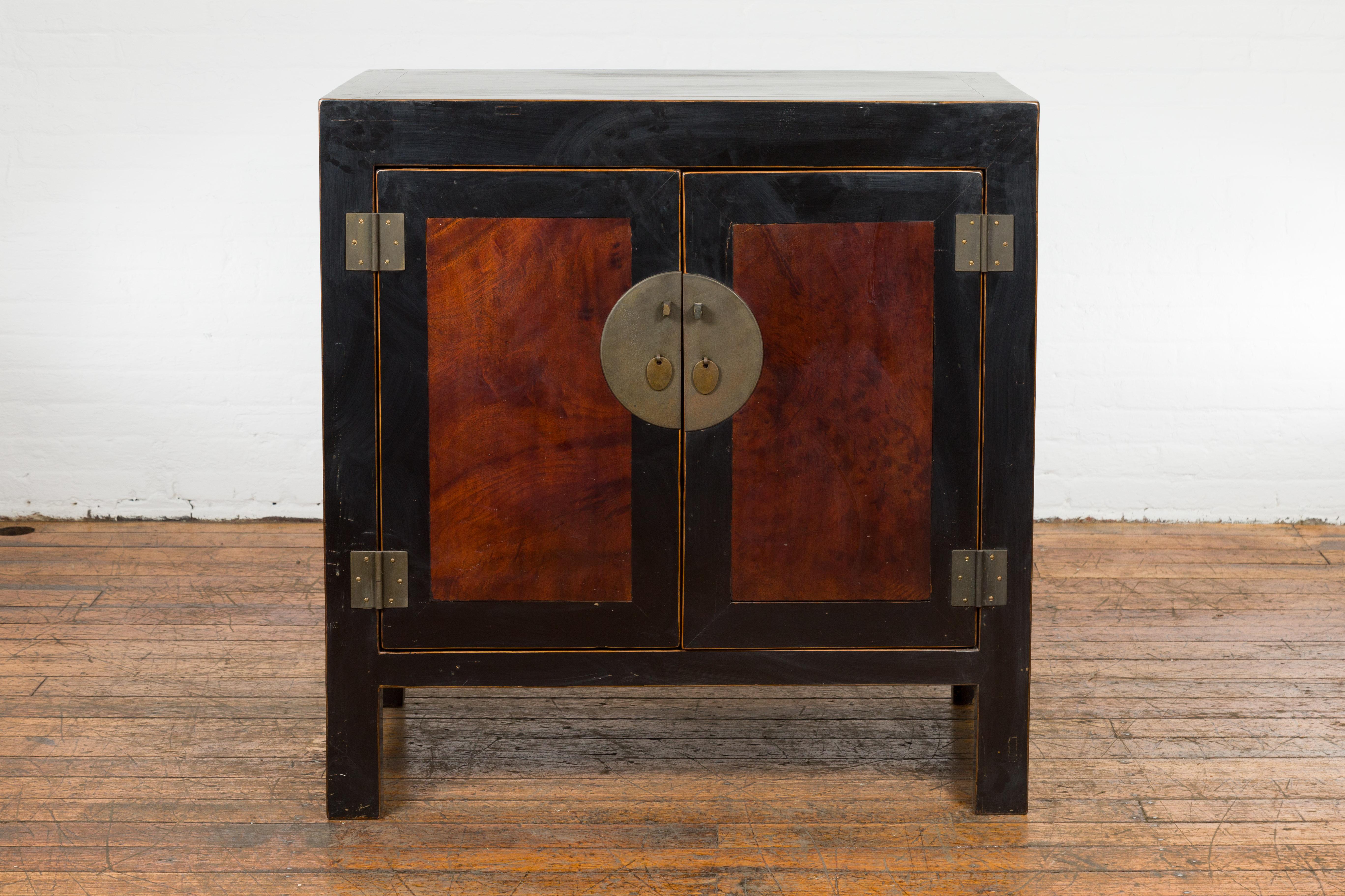 A Chinese Qing Dynasty period Hebei black lacquered two door low cabinet from the 19th century, with inset burl panels, golden trim and brass hardware. Created in Hebei, China during the Qing Dynasty period in the 19th century, this two-toned low