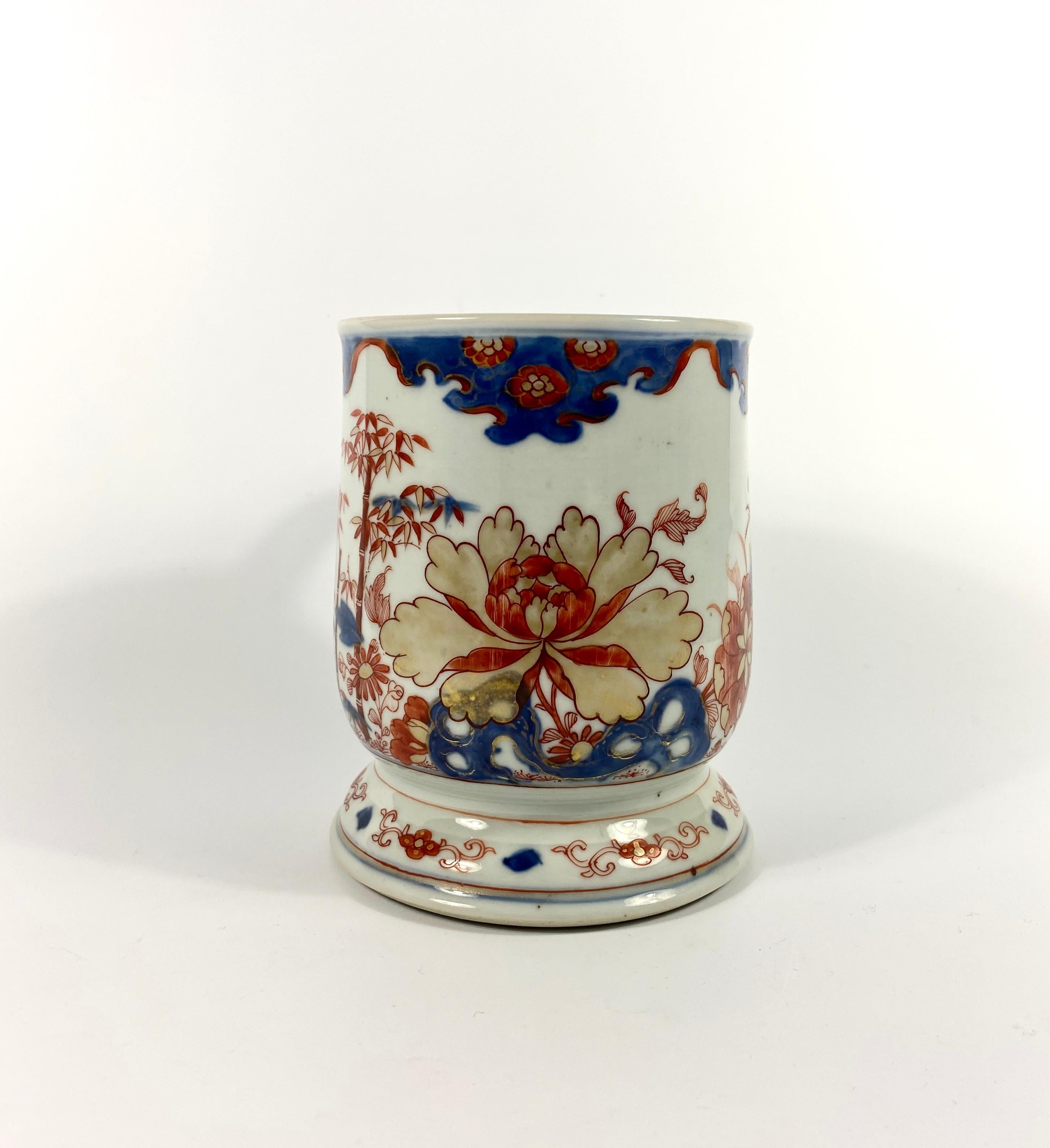 A large Chinese porcelain mug, circa 1720, Kangxi Period. The bell shaped mug, hand painted in the Imari style, with a large gilt flower head, rising above rocks, with bamboo growing to one side, and further plants to the other side.
Set upon a a