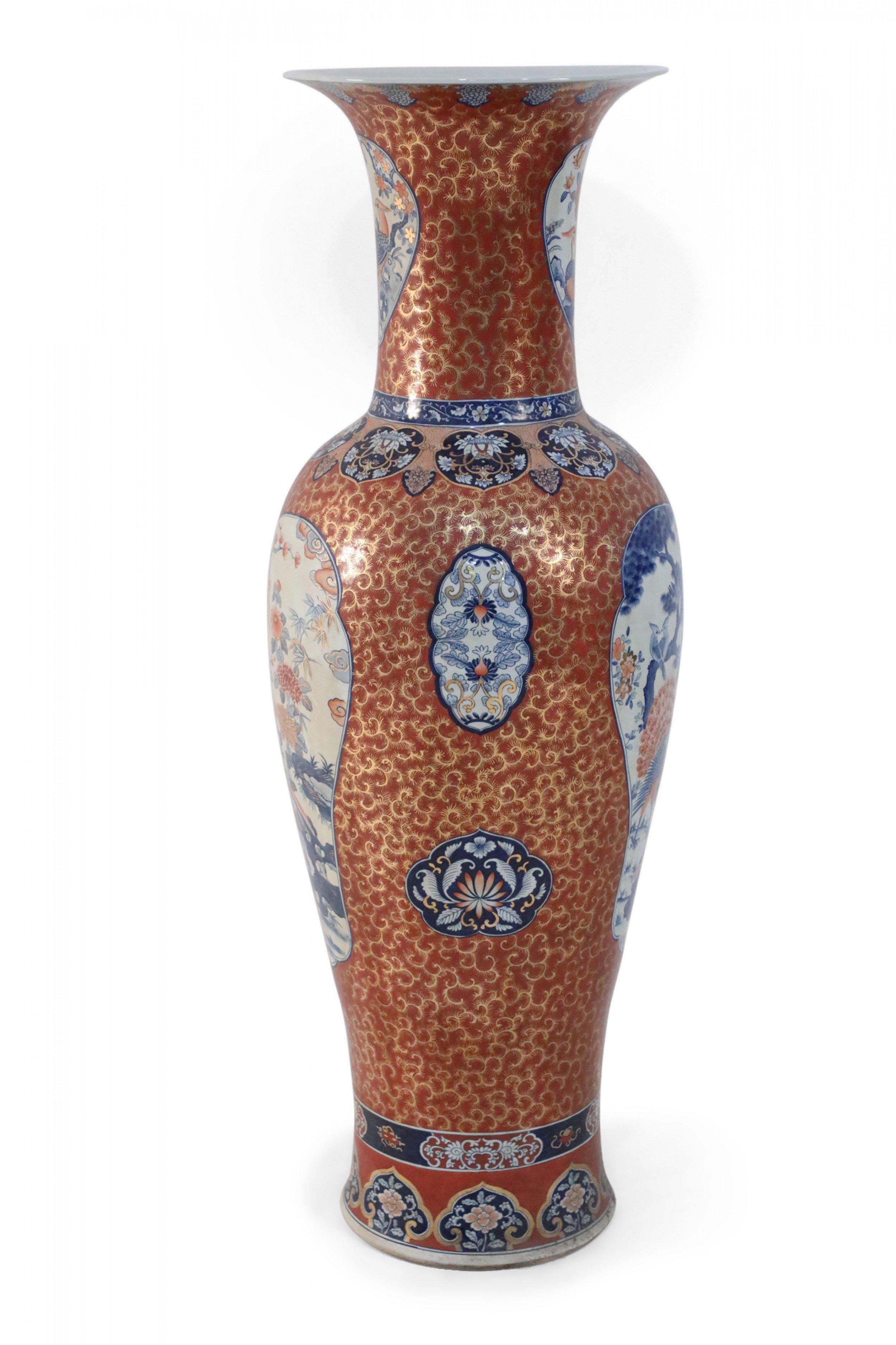 Vaso cinese monumentale da pavimento che celebra la ceramica giapponese Imari sia nella tavolozza che nel design, con medaglioni di scene naturali su un fondo arancione intricatamente decorato con un ricco e vorticoso motivo di viti dorate.

Condit: