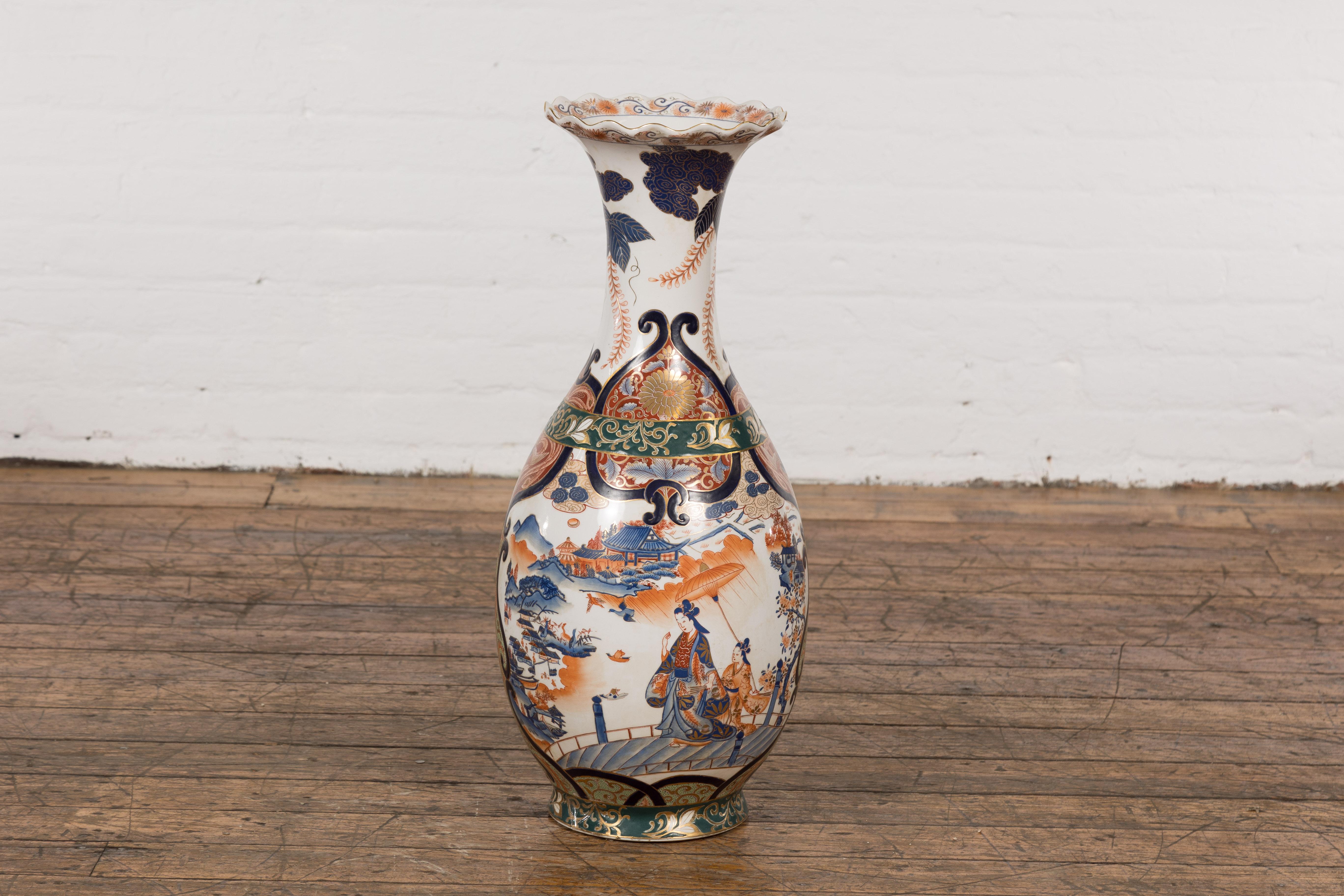 Vase d'autel vintage en porcelaine chinoise de style Imari, datant du milieu du 20e siècle, avec une sous-couche bleue, un sommet festonné, un décor orange, bleu et vert ainsi que d'élégantes dames, des architectures et des motifs de paysage. Ce