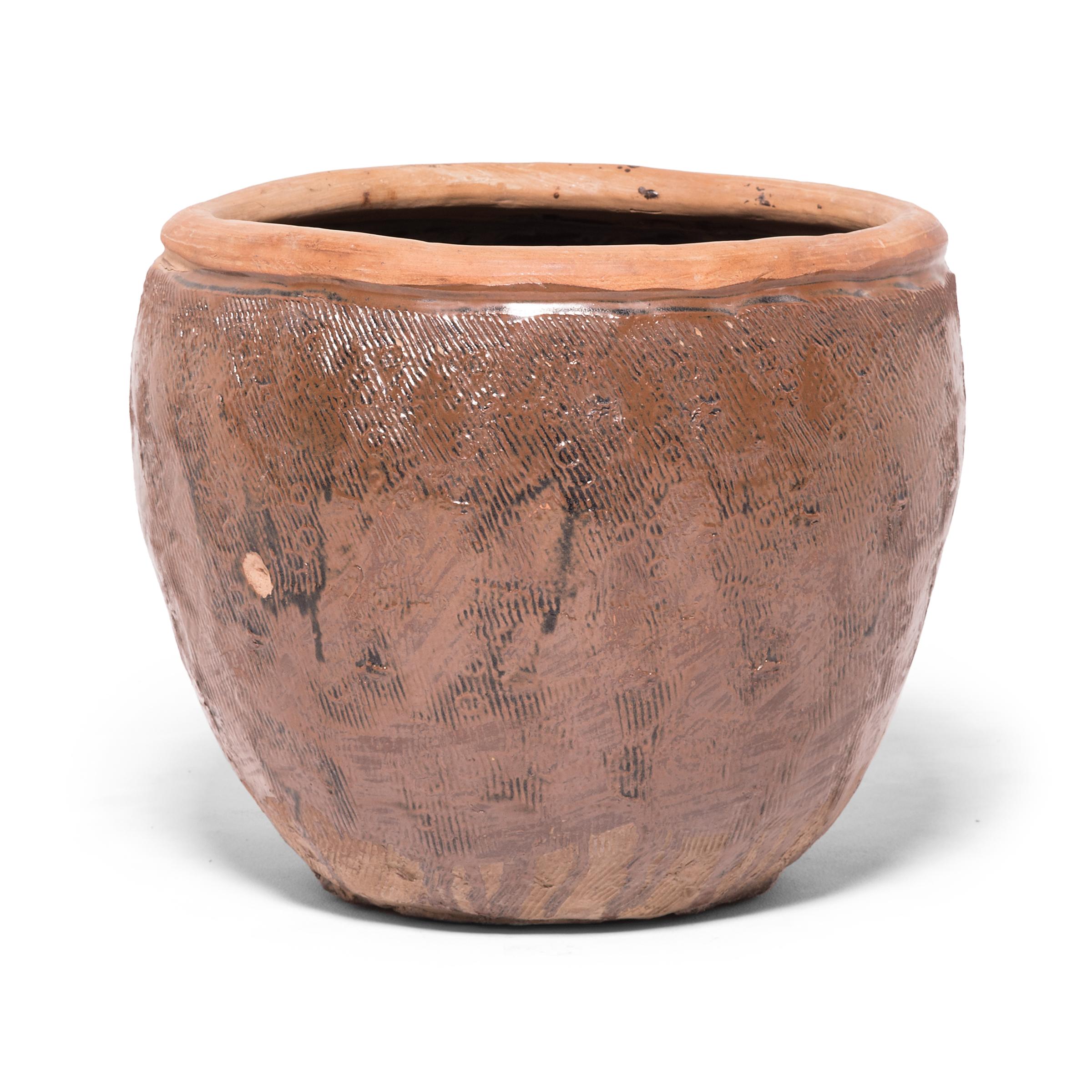 Once used to hold stockpiles of grain, this capacious terracotta jar is distinguished by the energetic incised pattern covering its exterior. Using a simple forked tool, the potter layered the vessel with dense etchings to enliven the simply shaped