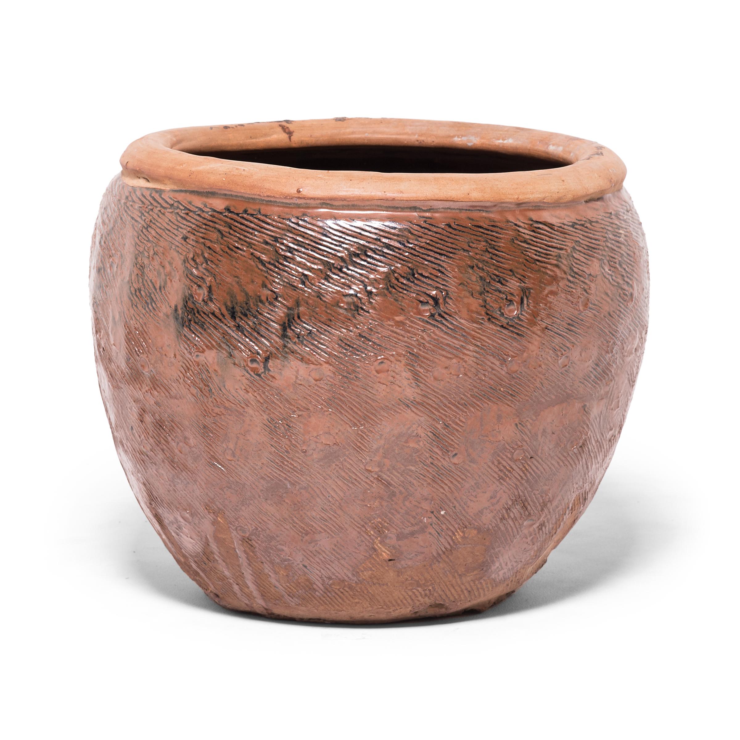 Once used to hold stockpiles of grain, this capacious terracotta jar is distinguished by the energetic incised pattern covering its exterior. Using a simple forked tool, the potter layered the vessel with dense etchings to enliven the simply shaped