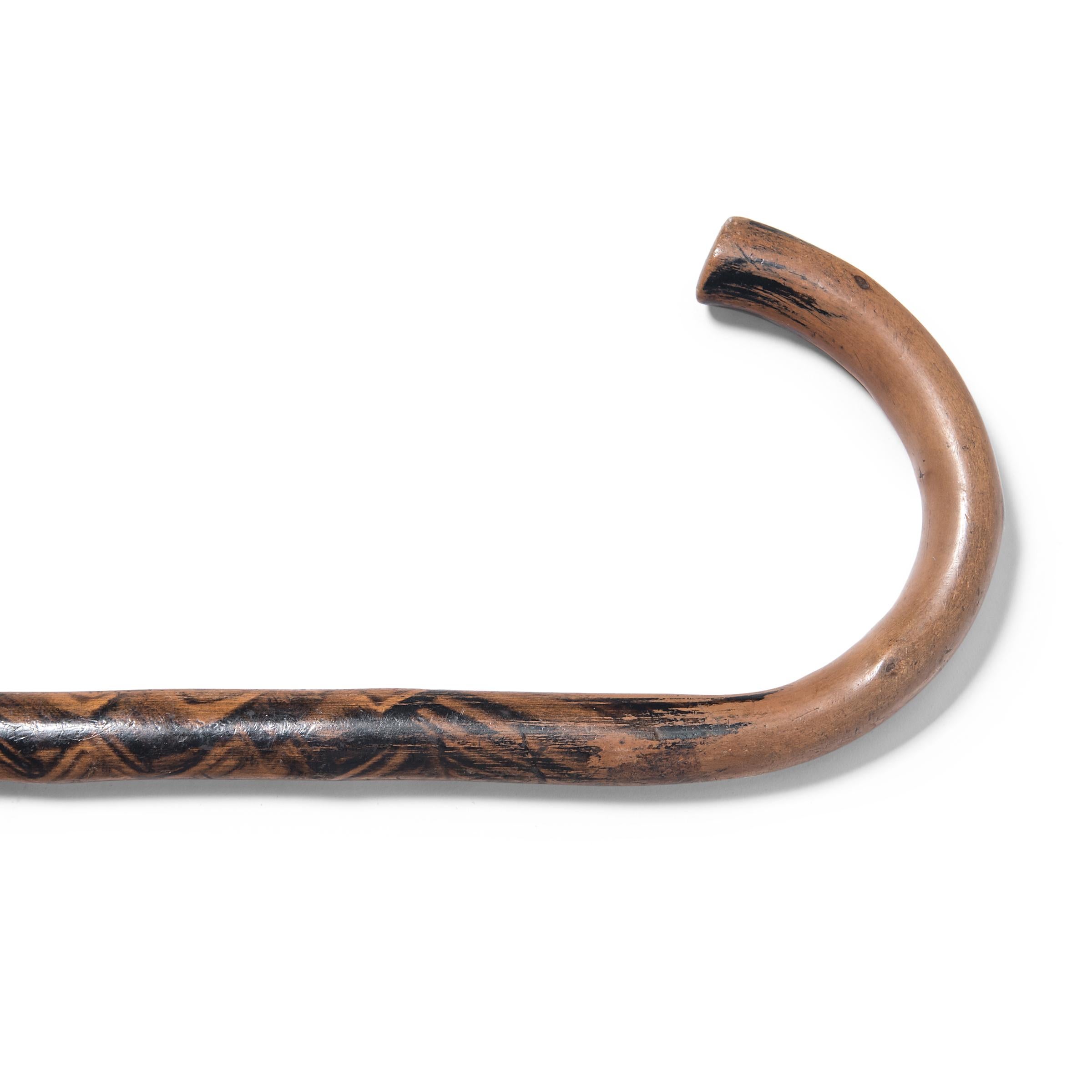 This late 19th-century walking stick from northern China is painted with swirling black ink in rhythmic brushstrokes. The curving handle has been burnished from a century of use, lending the staff soft warmth in contrast to the darkened surface.