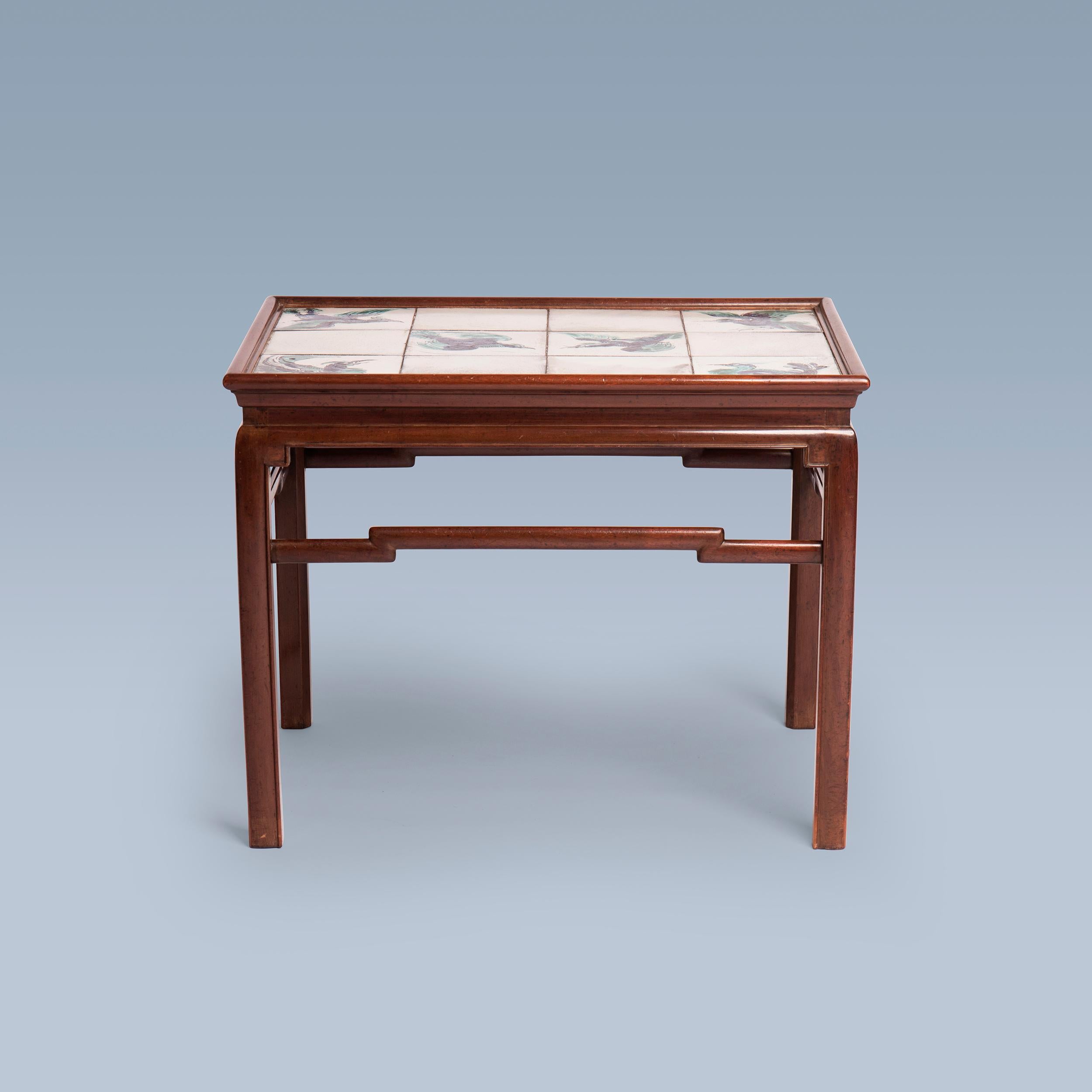 Cette table basse en acajou d'inspiration chinoise a été réalisée par l'ébéniste Frits Henningsen (1889-1965) dans les années 1930.
Le plateau de la table est décoré de carreaux uniques représentant les oiseaux chinois Fenghuang, également appelés