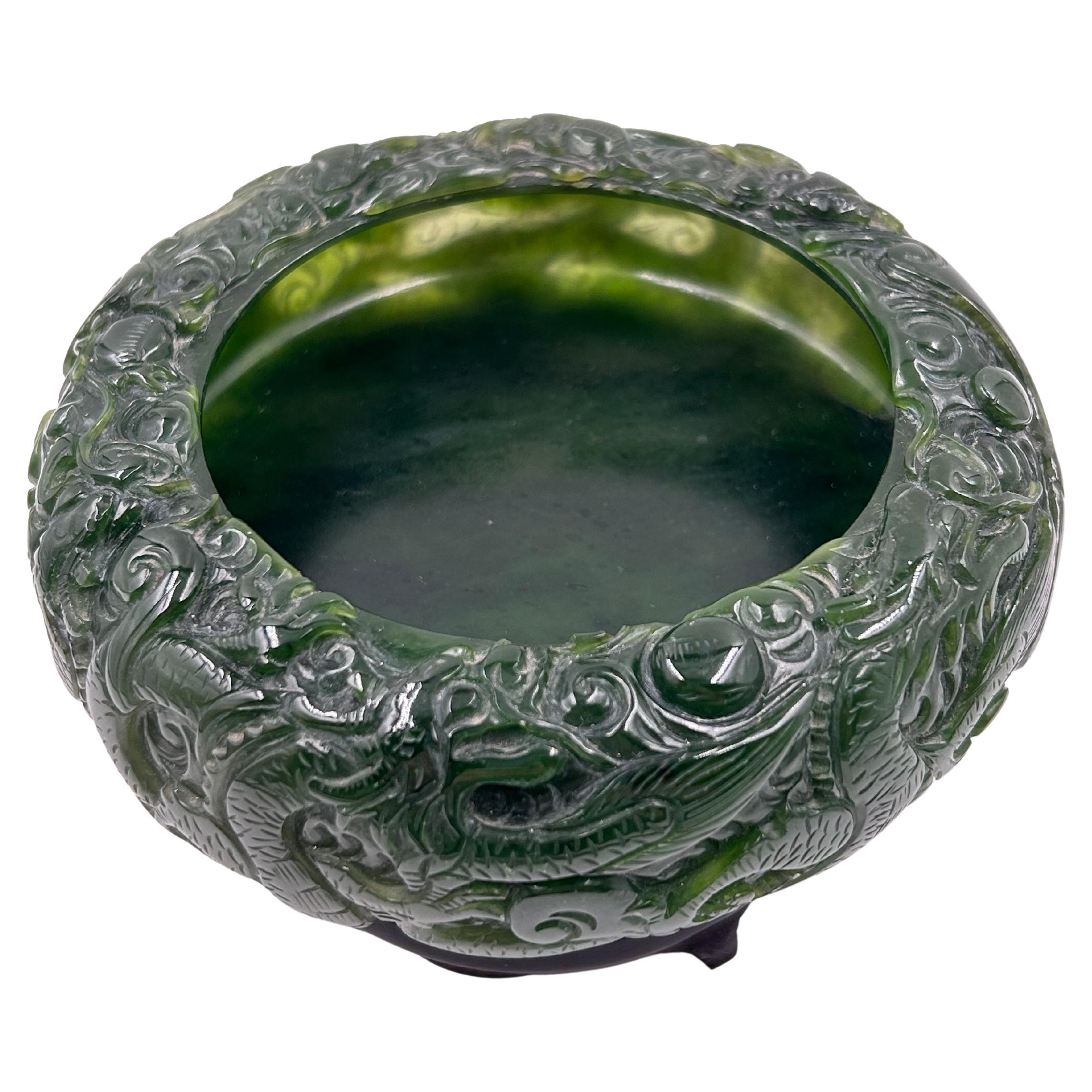 Chinese Carved Jade Bowl from the Qin Dynasty
Circular piece, finely hand-carved in deep green jade with lighter natural veins. It features an intricate continuous relief of imperial dragons among clouds, a traditional symbol of power and prosperity
