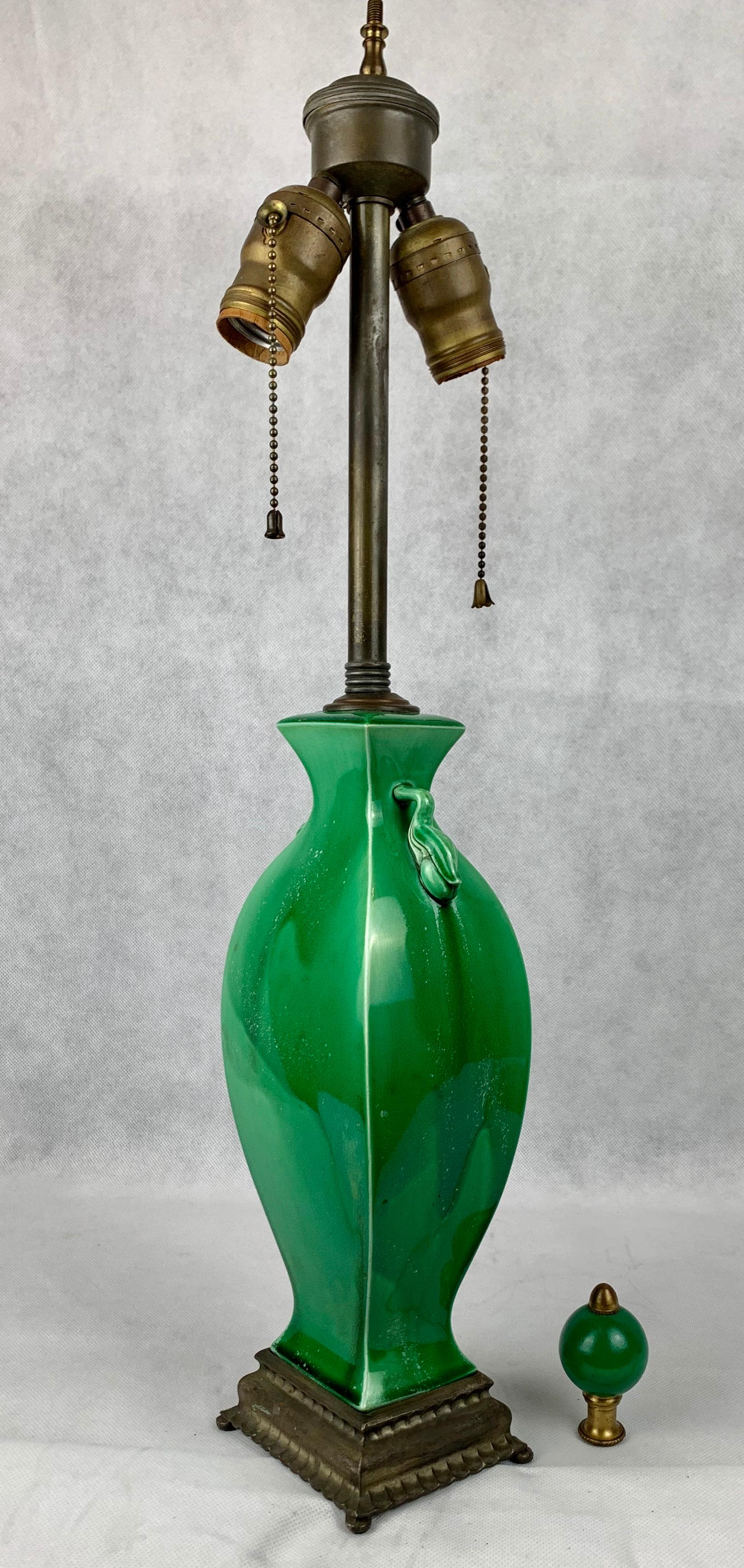 Jade green Chinese porcelain two handled lamp with a matching finial. The shape is Classic Chinese. The handles are pieces of fruit with leaves. The lamp has a double light cluster and has been mounted on a rectangular metal base with small feet.