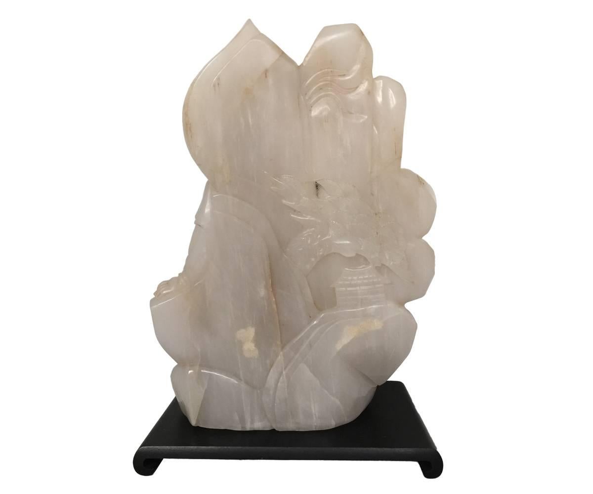 This well carved figure depicts the Quan Yin holding a vase of her tears and seated near the mountain edge above the the ocean. Next to her is a child with hands in the praying position and the face turned outward. The jade is of pale color and has