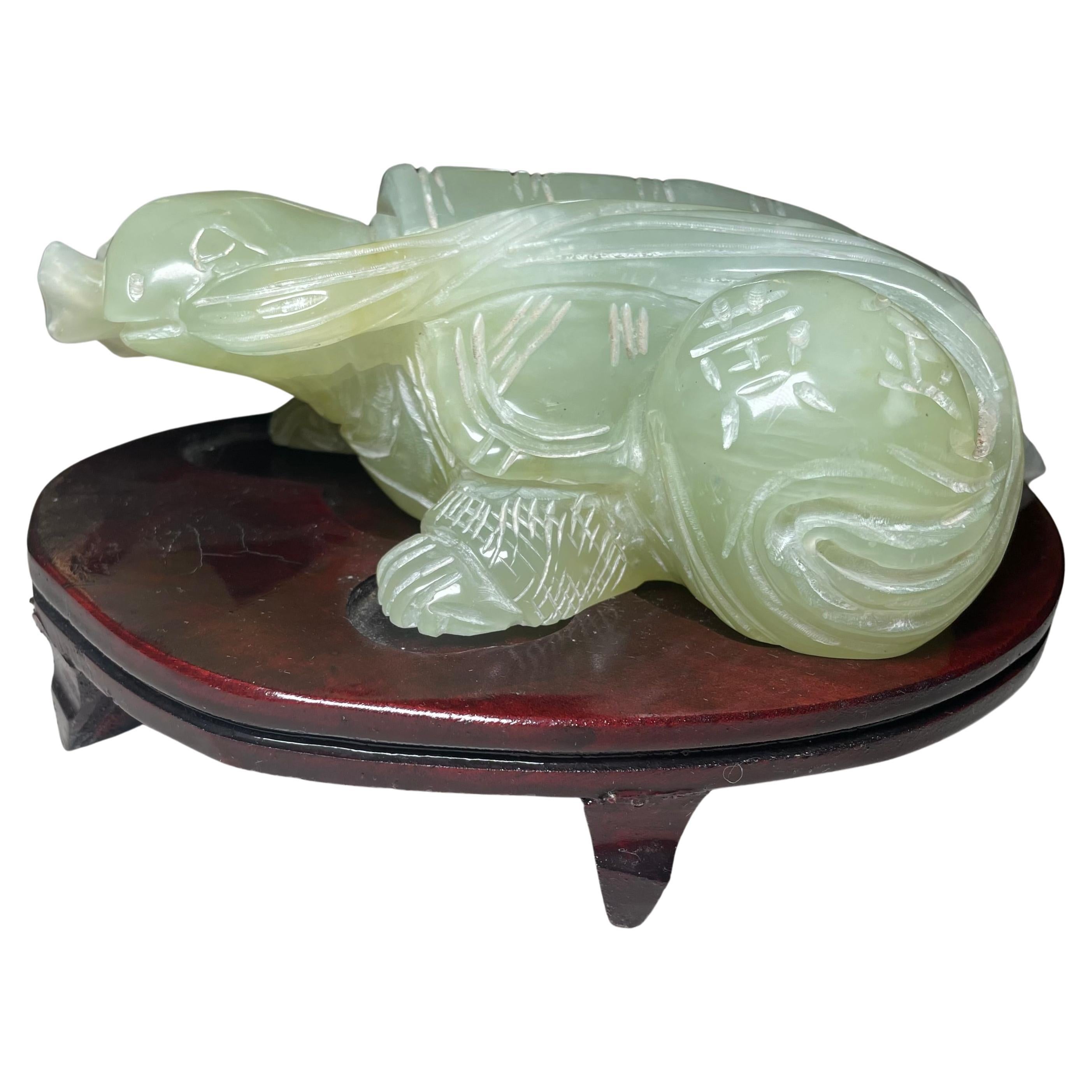 Scultura di tartaruga cinese in giada con supporto. Raffigura una pesante tartaruga di giada verde chiaro traslucida intagliata a mano con un pezzo di seta in bocca che tira un rotolo di seta. La figura di tartaruga in giada è sostenuta da un