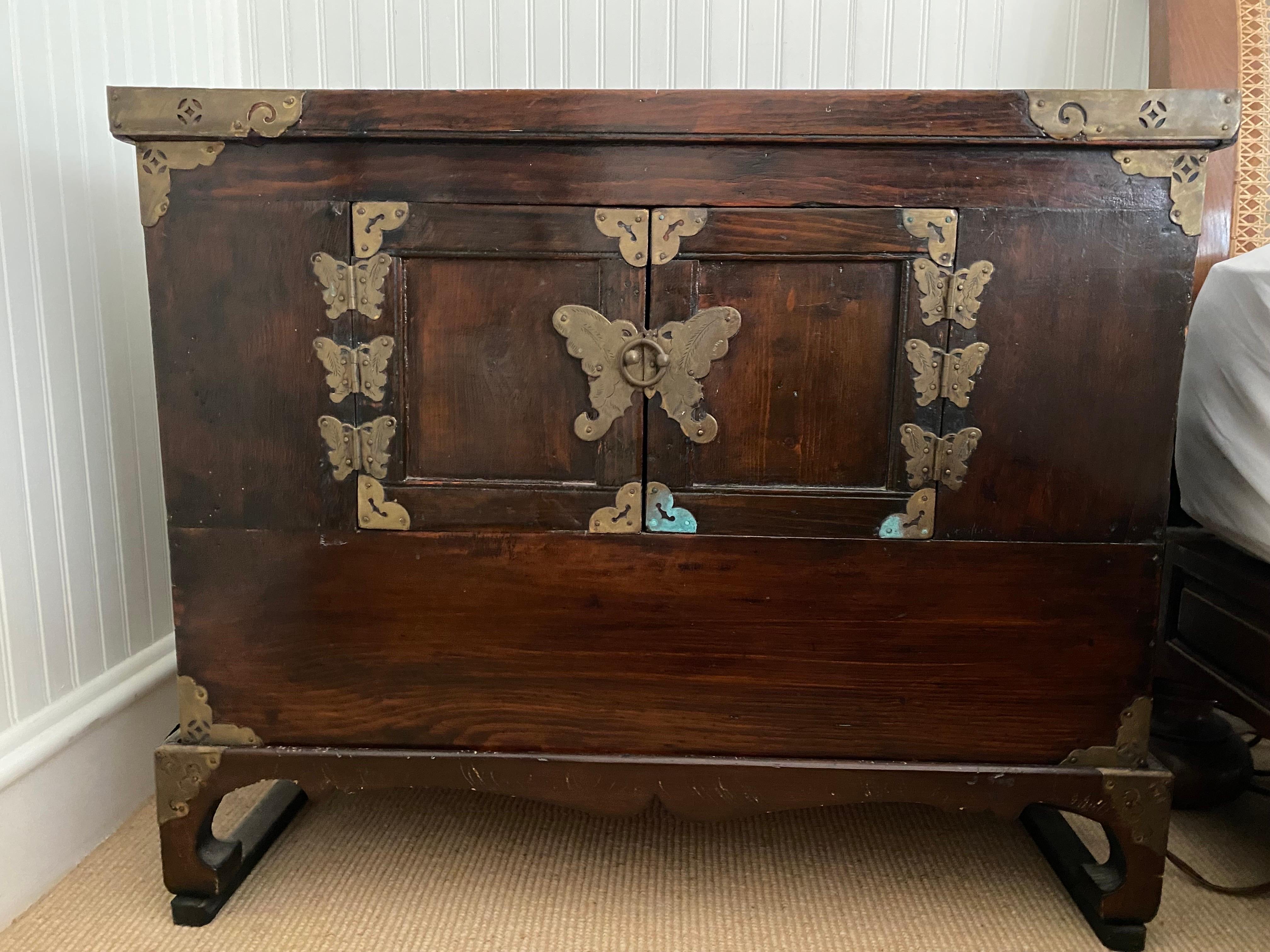 Chinese Kang Low Two Door Cabinet on Stand, 19th Century
A lovely wooden box with elaborate brass butterfly hardware on two doors which open to a storage area, sitting on a small stand.  General wear consistent with age and use. good overall