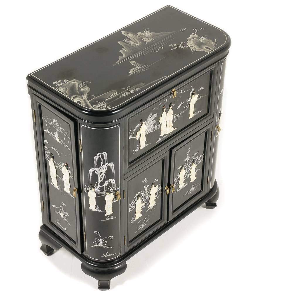 An unusual vintage Chinese liquor cabinet or bar, the deep black lacquer finish embellished with bas-relief painted scenes and carved polished hardstone figures.

The top opens to reveal a fitted fold-down surface for preparing cocktails; the