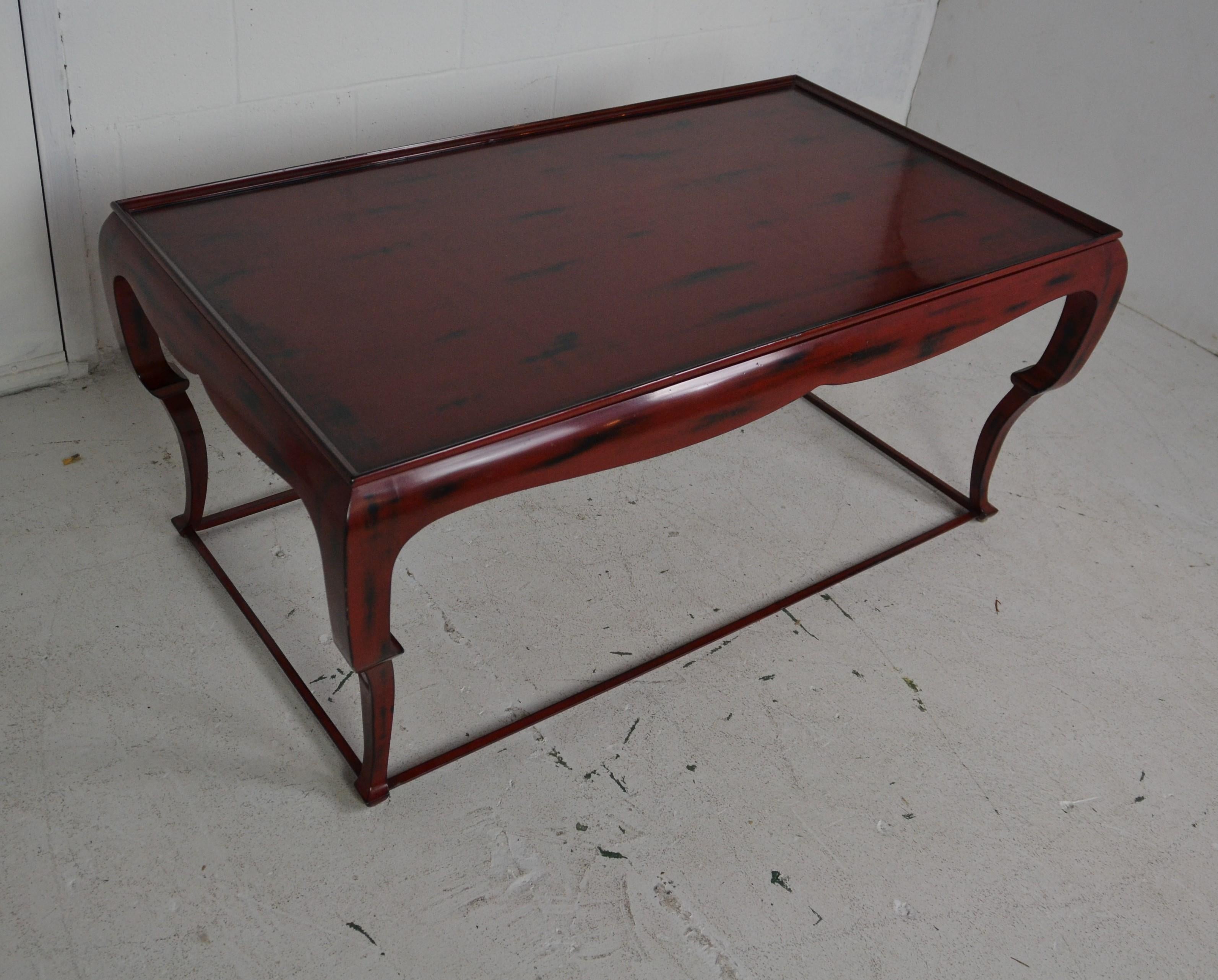 A Chinese red lacquer coffee table with smokey black decorations. A cabriole style leg with pad feet and a floor level stretcher bar.