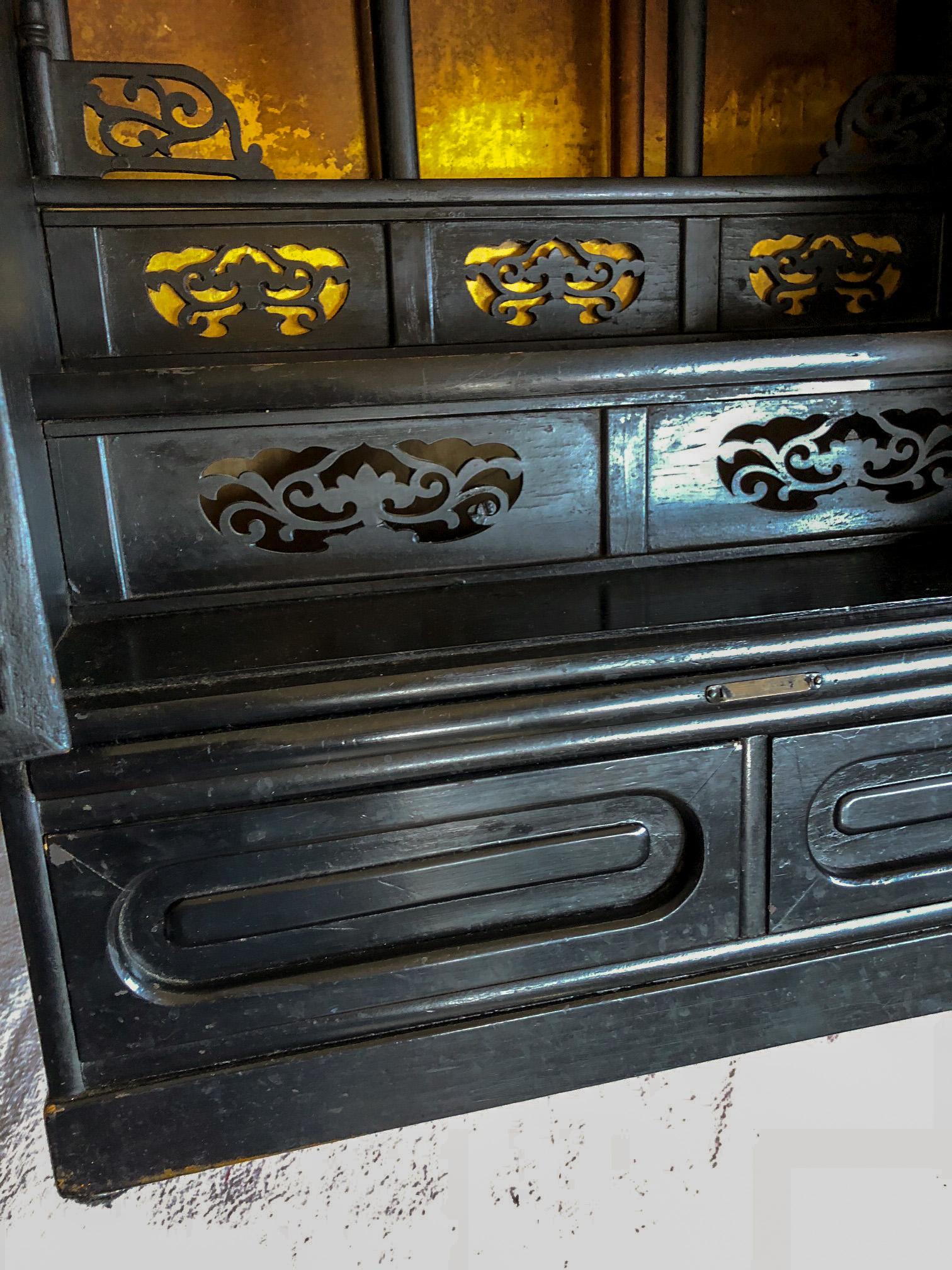 Wonderful 1920s-1940s Chinese elmwood black lacquer reliquary cabinet with bifold doors, two drawers, and a pull-out tray. Note the gold leafed interior with Chinoiserie fretwork. Reliquary would make a lovely side table by an armchair. Allover