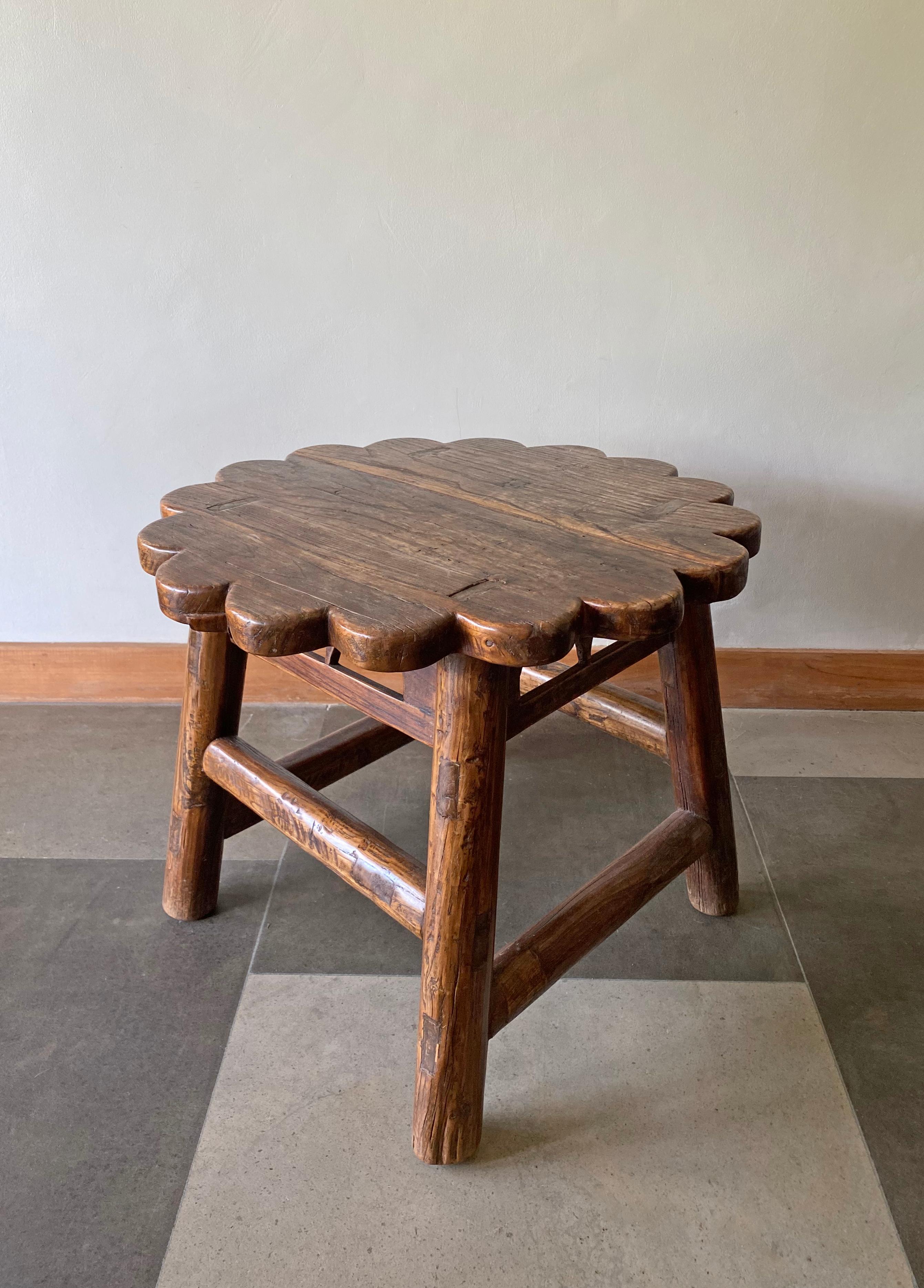 This antique elm wood lacquered stool comes from China's Hubei province. Crafted using only wooden joints it features a floral shape and subtle detailing across its upper horizontal joints. 

Dimensions: Height 49.5cm x Diameter 59cm.