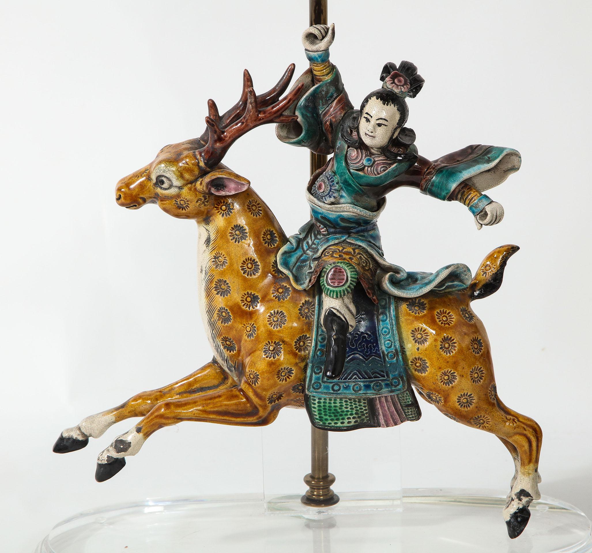 The porcelain figure wearing traditional clothing riding a stylized deer. Stamped on reverse and now mounted on a plexiglass base as a lamp.