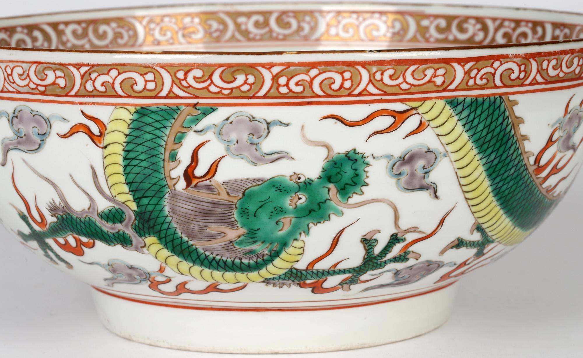 A large and impressive Chinese Qing porcelain punch bowl decorated in the famille verte palette with scrolling dueling dragons and dating from the early to mid 19th century. The bowl stands raised on a narrow rounded foot and is hand decorated in