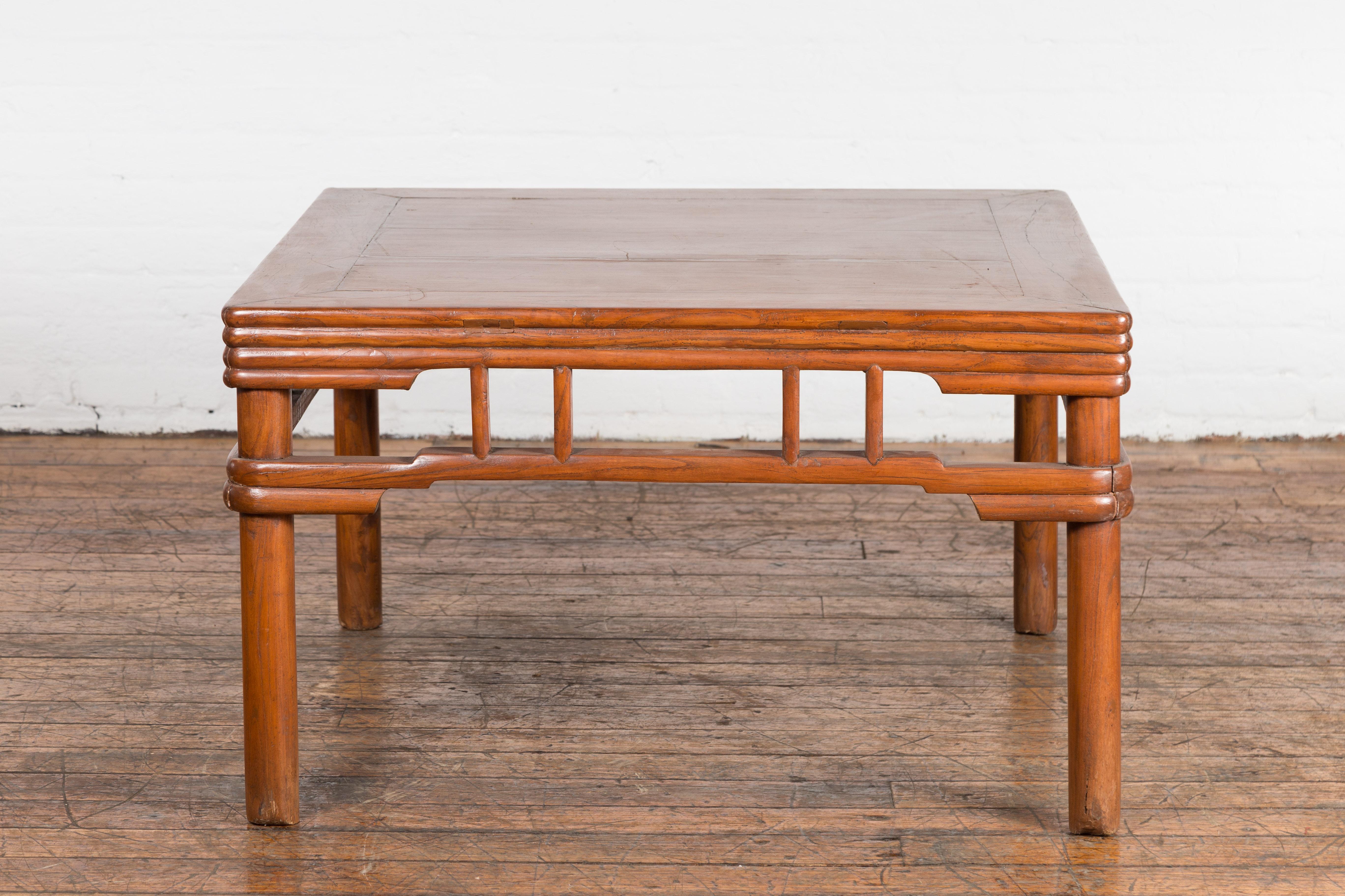 A Chinese late Qing Dynasty period natural elm coffee table from the early 20th century, with open apron, pillar strut motifs, humpback stretchers and reeded accents. Add a touch of elegance and sophistication to your living space with this Chinese