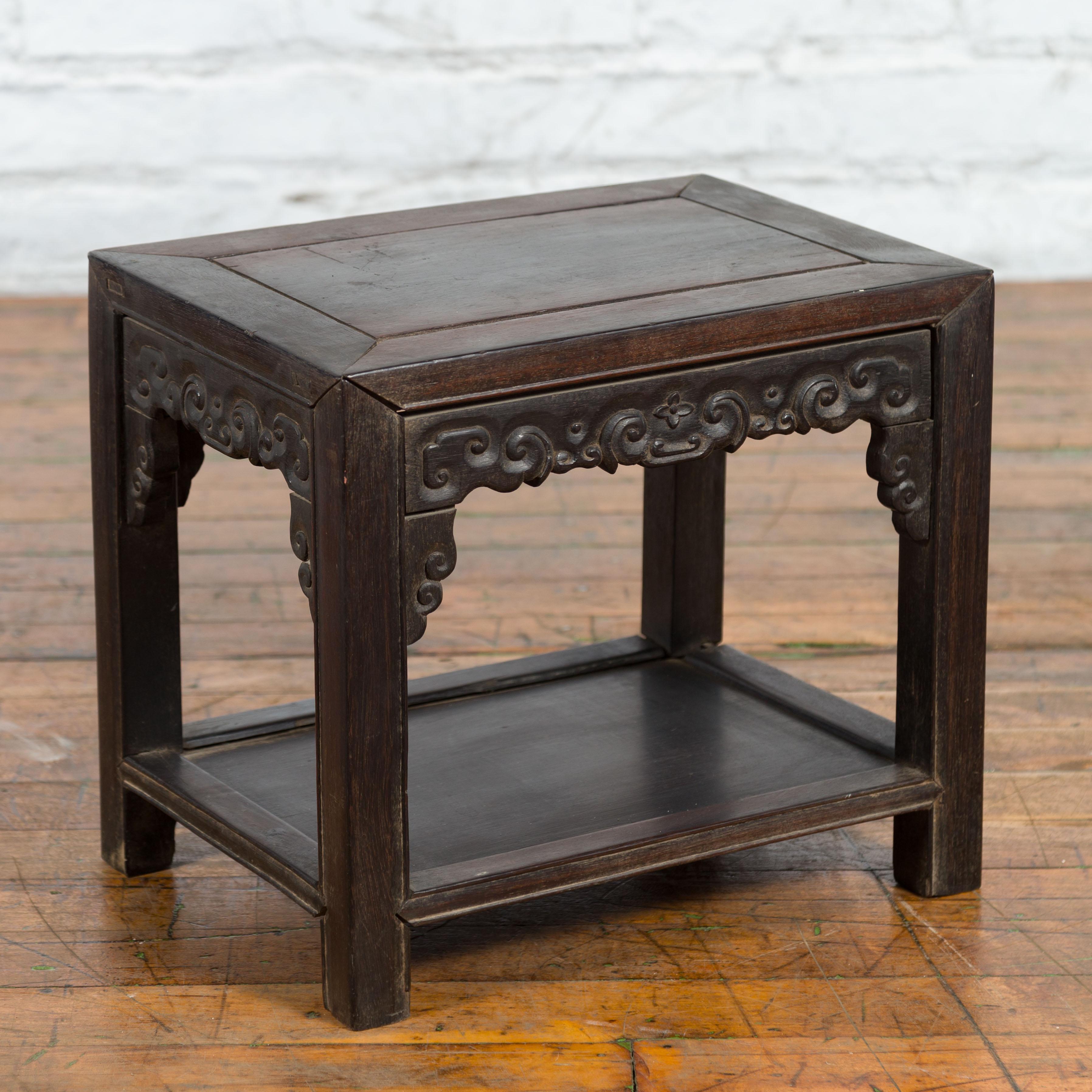 A Chinese Late Qing Dynasty period dark stool from the early 20th century with carved apron and lower shelf. Created in China during the late Qing Dynasty period in the early years of the 20th century, this stool would also be wonderful used as a