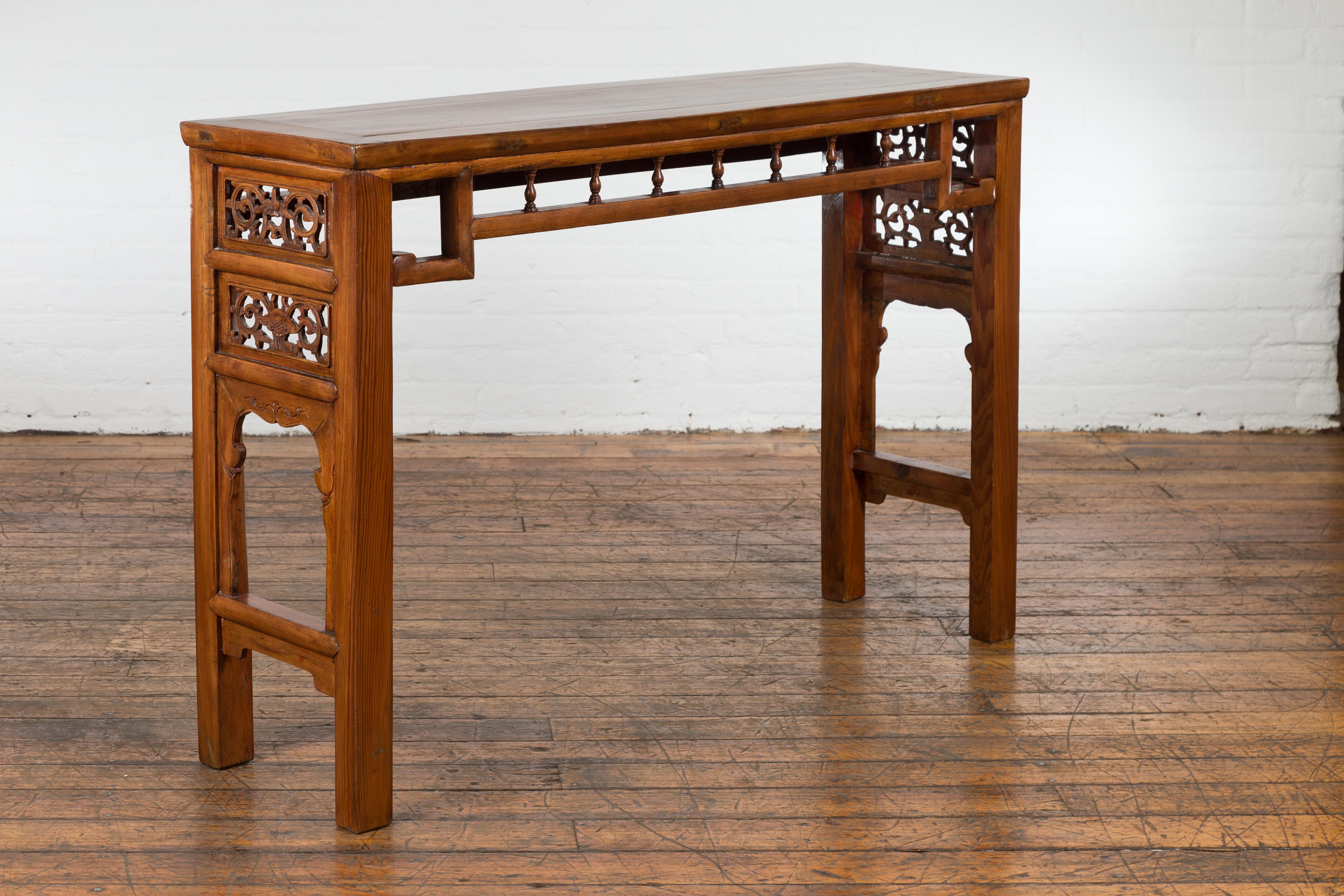 A Chinese late Qing Dynasty period altar brown lacquered console table from the early 20th century with scrolling foliage-carved side panels, humpback stretchers, petite turned baluster motifs on the apron, newly and professionally refreshed. This