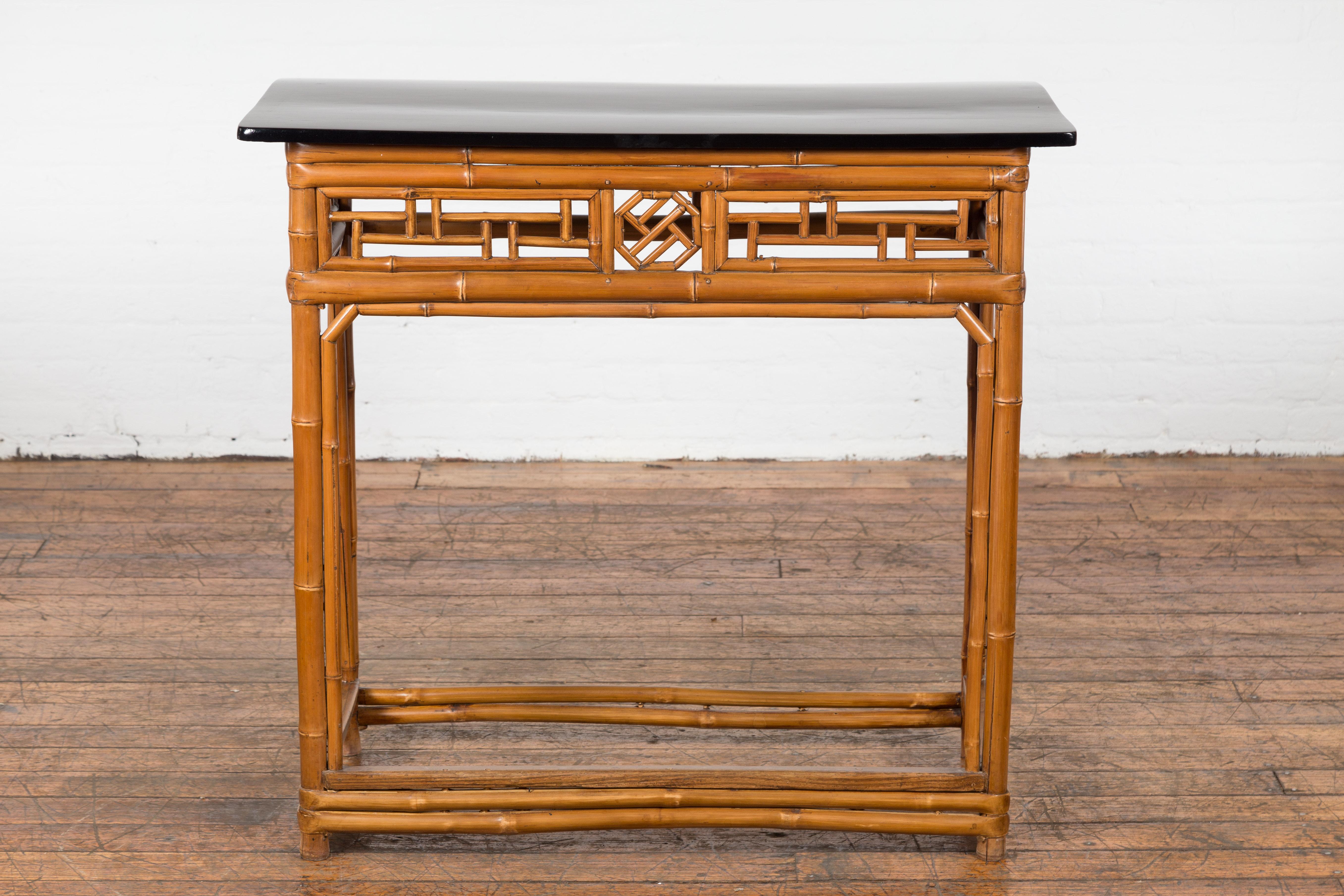 A Chinese late Qing Dynasty period bamboo console table from the early 20th century with black lacquered top, geometric apron, four straight legs and side stretchers. This Chinese late Qing Dynasty period bamboo console table from the early 20th