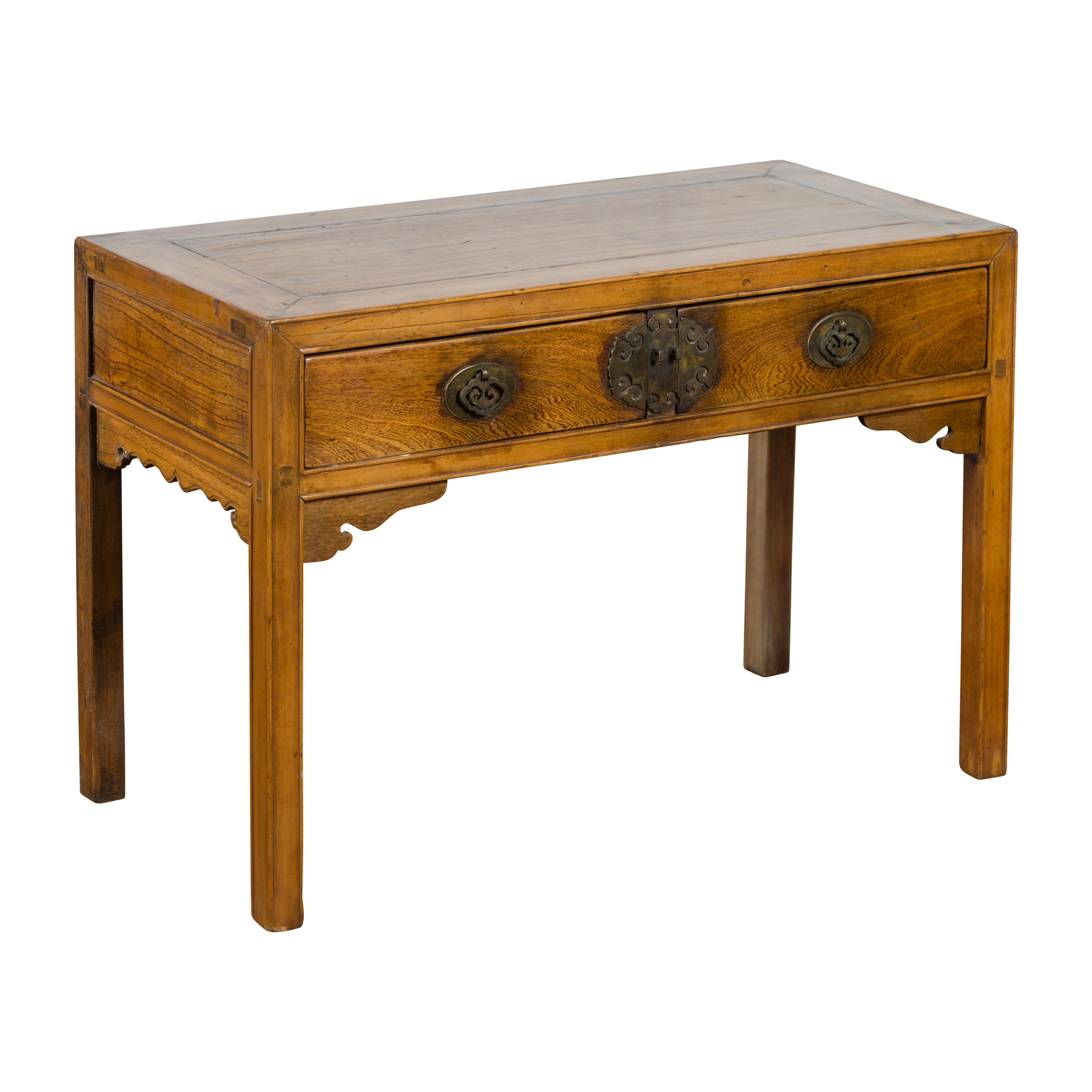 A late Qing Dynasty period Chinese elm wood desk from the early 20th century, with two drawers, brass hardware and carved spandrels. Created in China during the late Qing Dynasty period in the early years of the 20th century, this elm wood desk