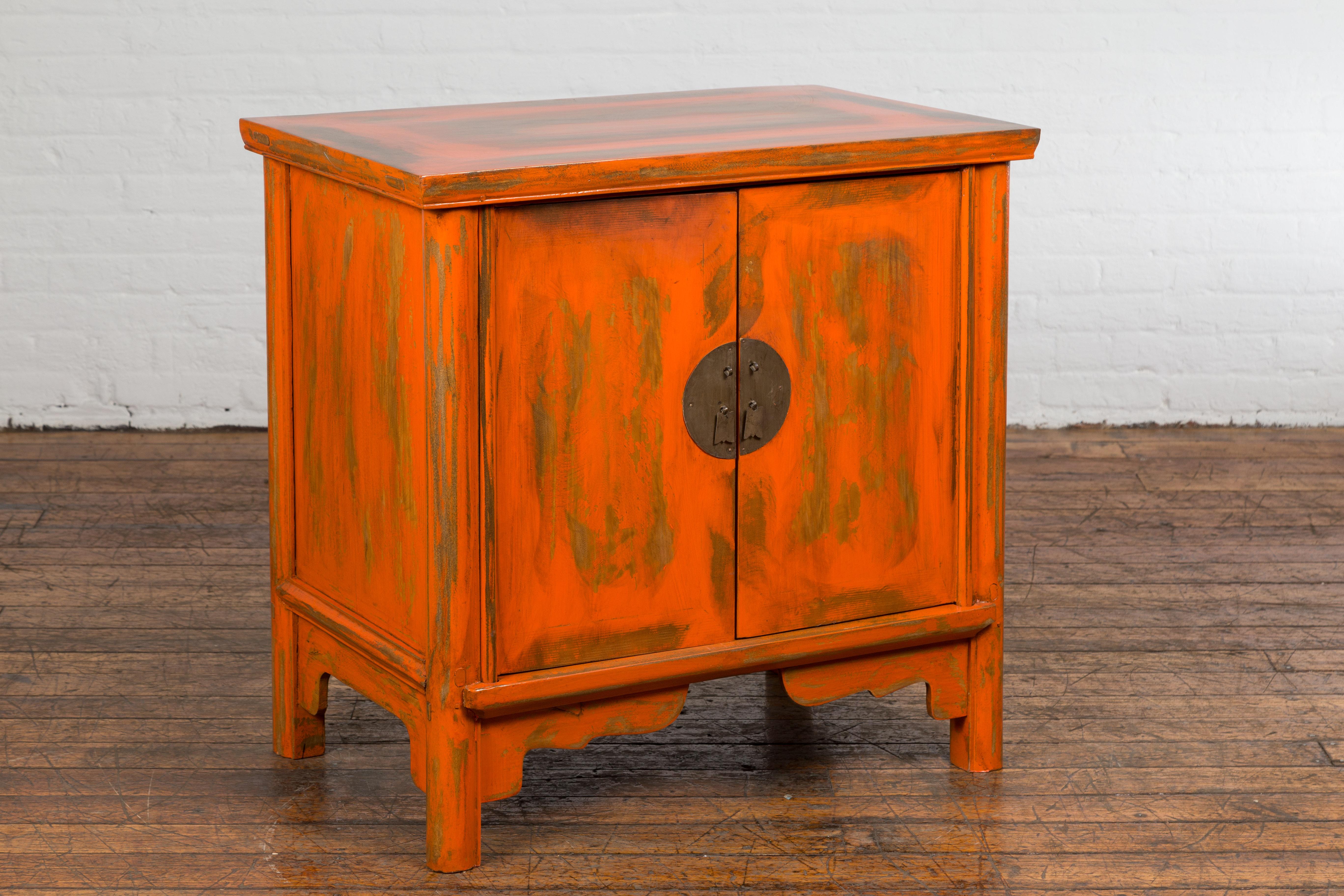 A Chinese late Qing Dynasty period elmwood side cabinet from the early 20th century with new custom distressed orange lacquer, two doors, brass hardware, carved spandrels and straight feet. This Chinese late Qing Dynasty period elmwood side cabinet