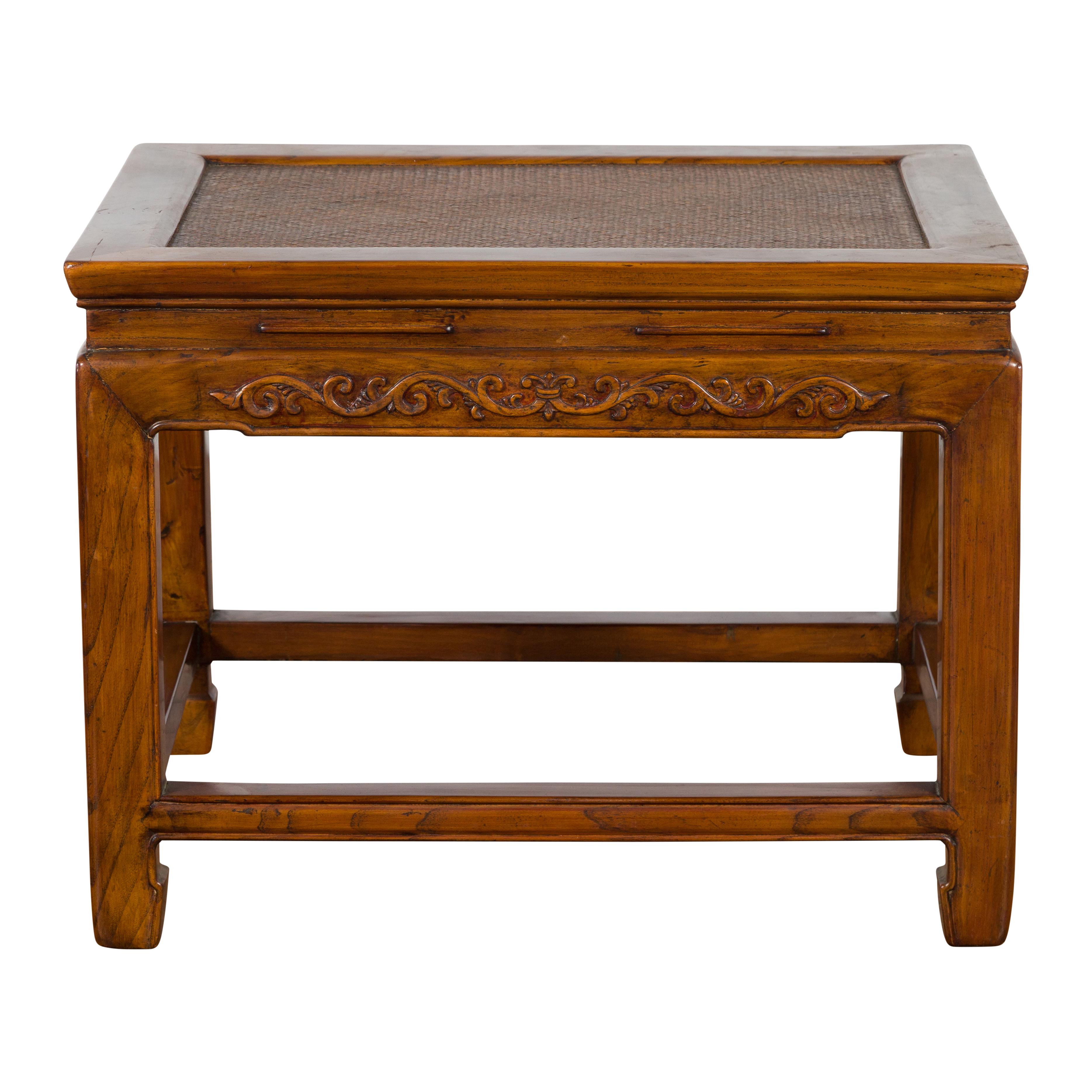 A Chinese late Qing Dynasty period elm wood side table from the early 20th century with woven rattan top, waisted apron and low-relief carved frieze. Created in China during the later years of the Qing Dynasty period in the early 20th century, this
