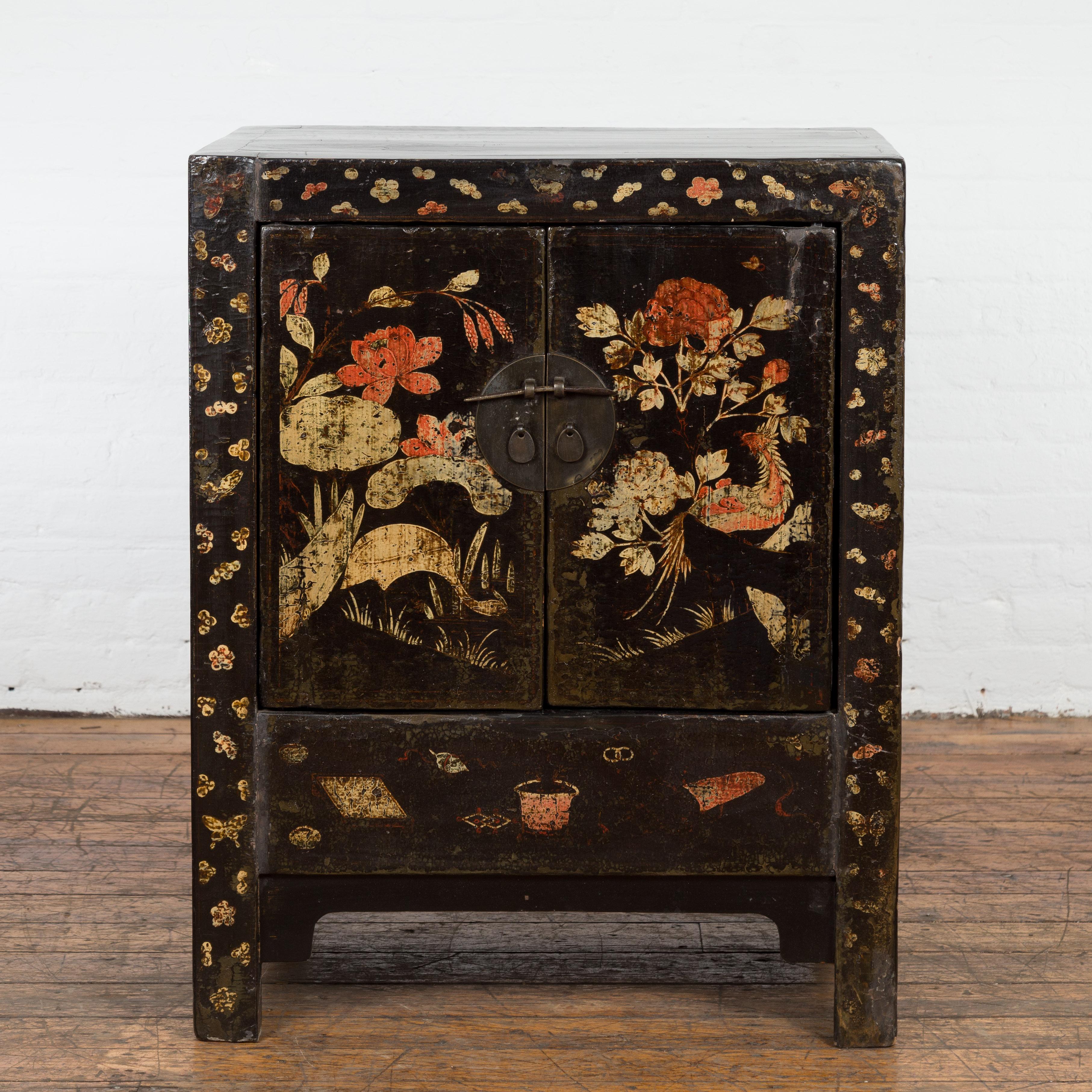 A Chinese late Qing Dynasty period dark brown lacquered bedside cabinet from the early 20th century, with hand painted cream and orange dragon, bird and floral motifs, two doors, traditional bronze medallion hardware, straight legs, carved apron and