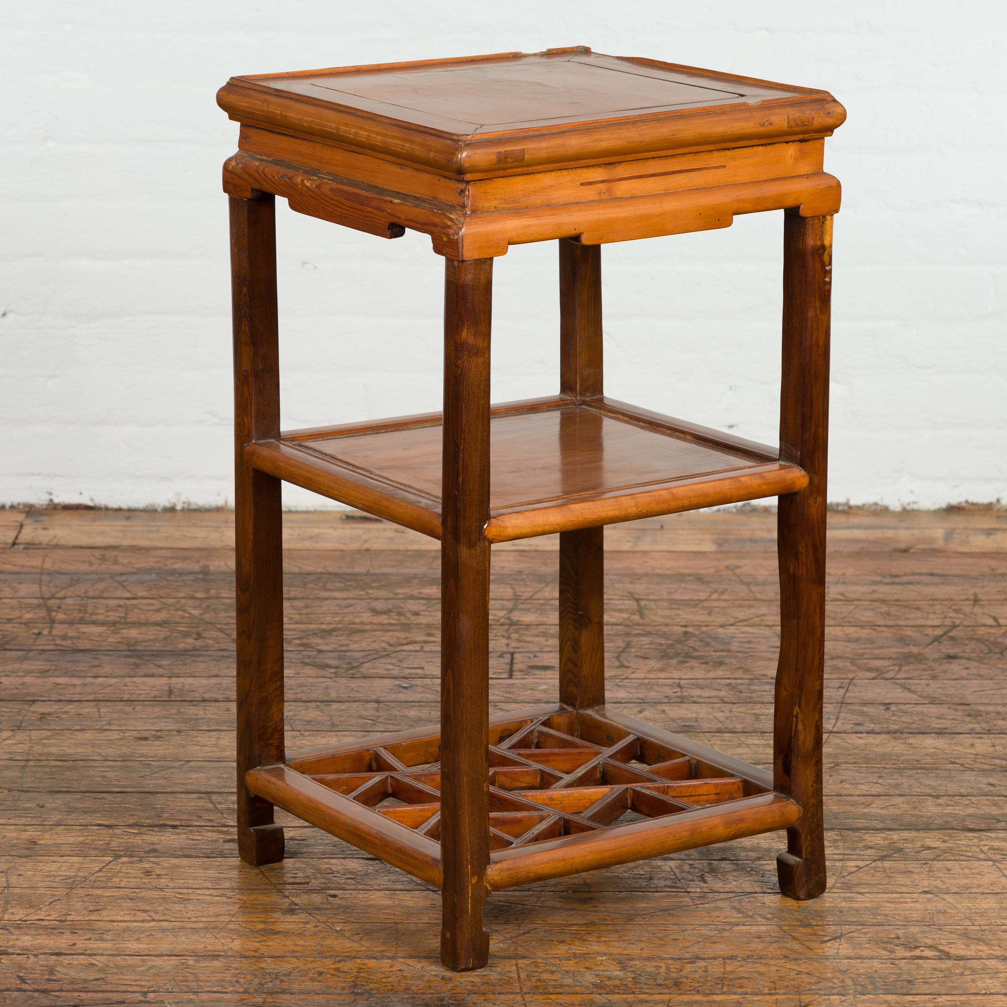 A Chinese late Qing Dynasty period lamp table from the early 20th century, with carved apron, shelves, cracked ice patterns and horse hoof feet. Created in China during the late Qing Dynasty period in the early years of the 20th century, this lamp