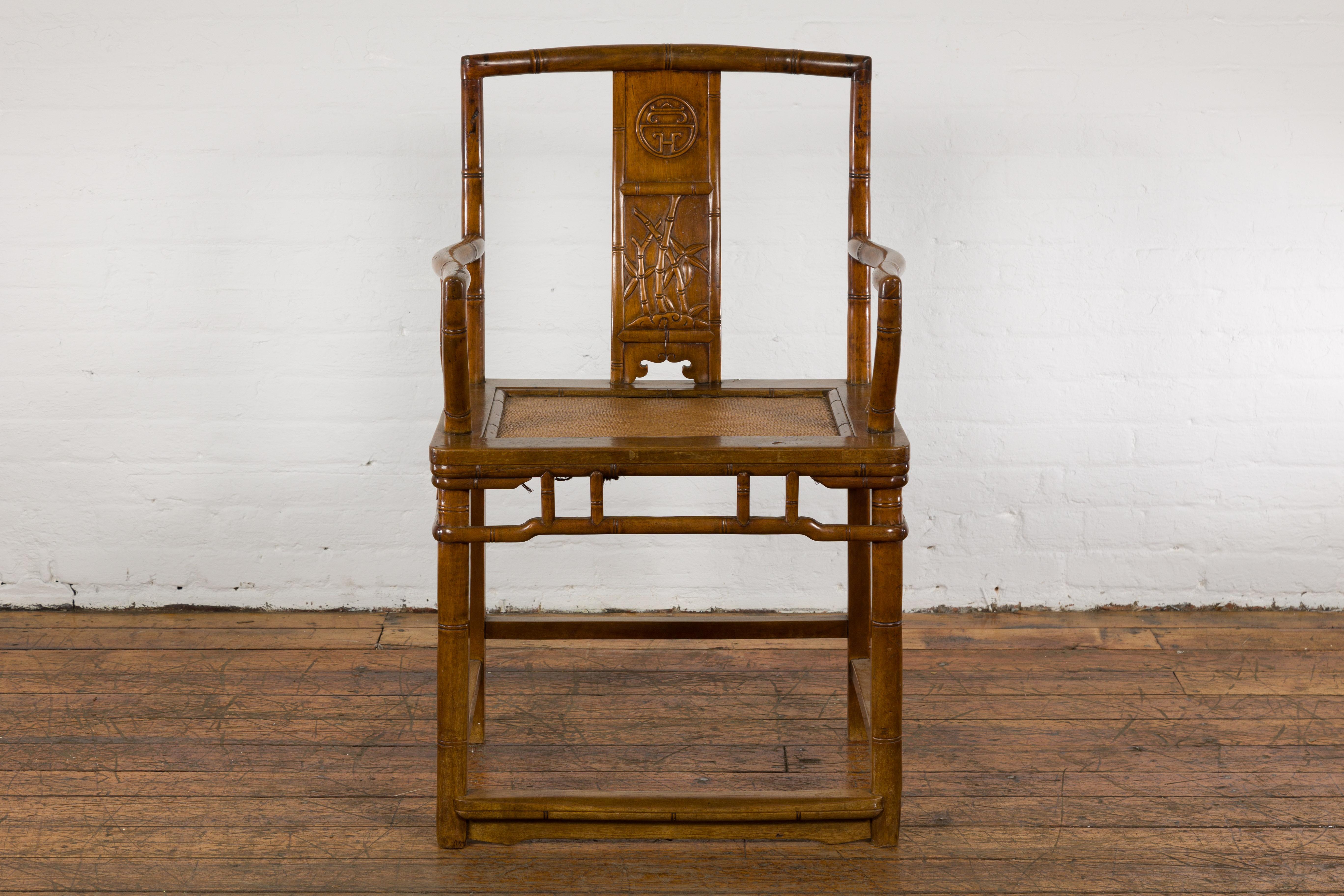 A Chinese late Qing Dynasty period wooden armchair from the early 20th century, with carved splat, sinuous arms, rattan seat and pierced pillar strut decorated apron. This antique piece showcases a beautiful fusion of form and function, making it an