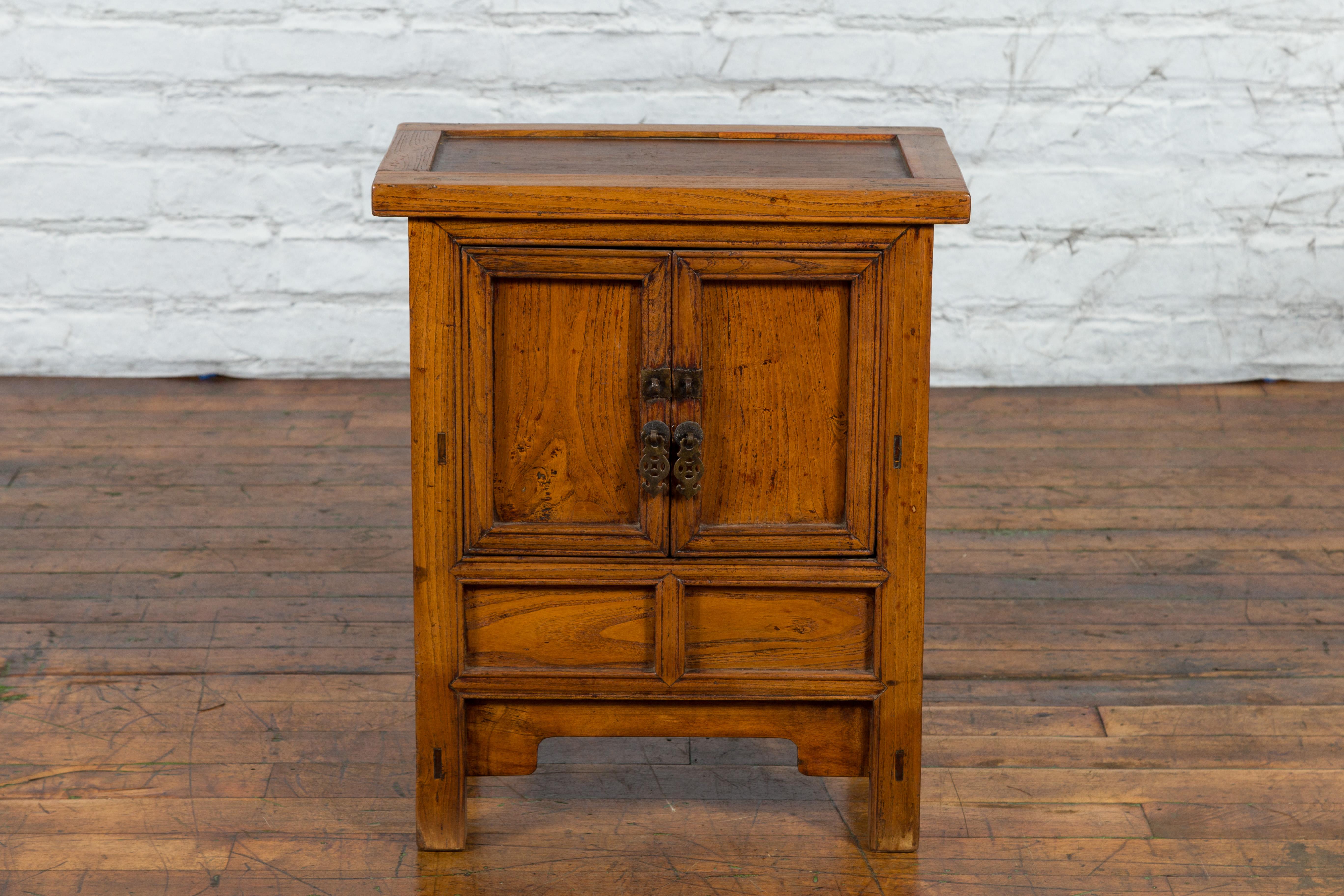 A Chinese late Qing Dynasty period wooden bedside cabinet from early 20th century, with two doors, carved apron and weathered patina. Created in China during the late Qing Dynasty in the 20th century, this wooden bedside cabinet captures the