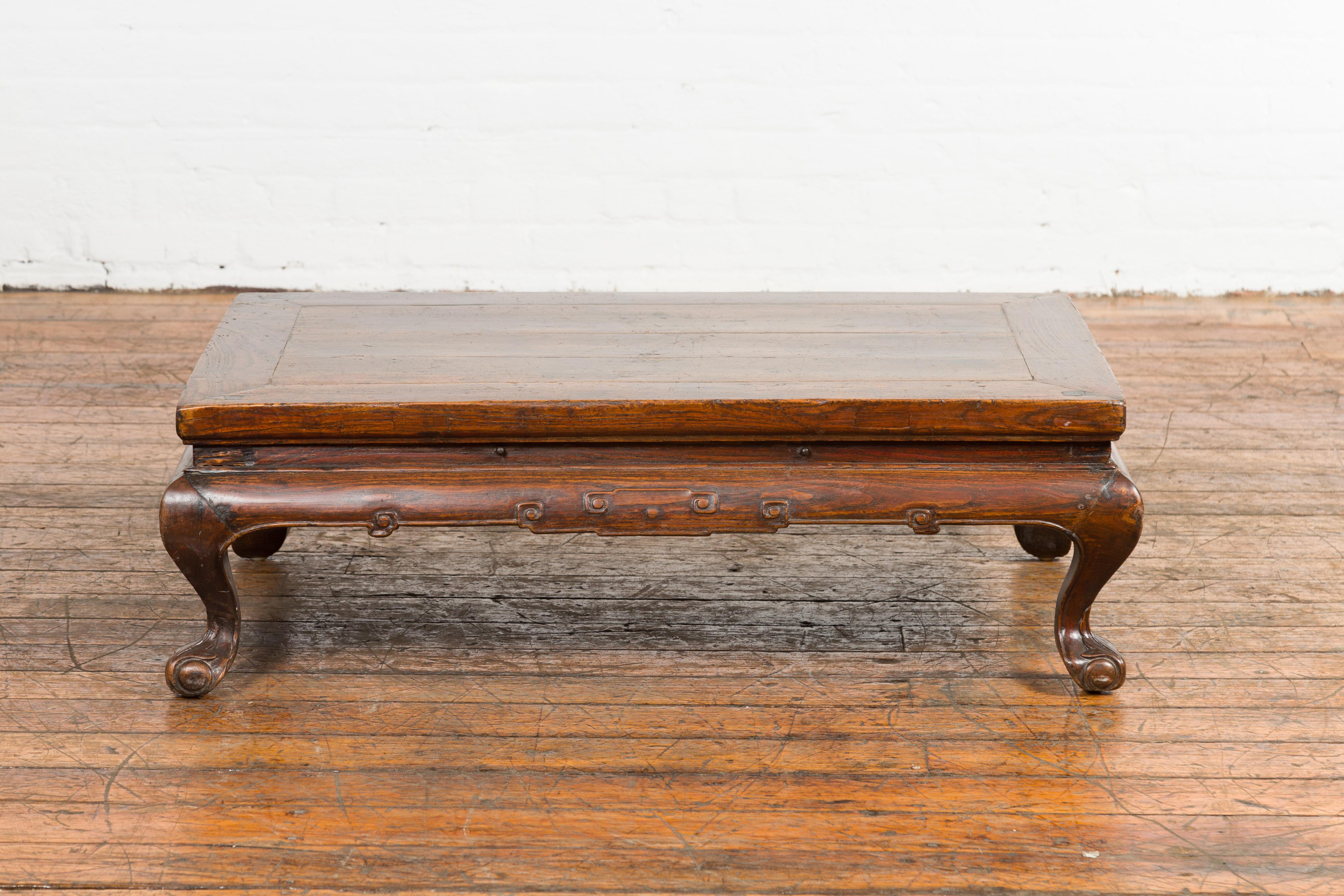 A Chinese late Qing Dynasty period low Kang coffee table from the early 20th century, with carved apron and cabriole legs. Step into the world of antique Chinese craftsmanship with this coffee table, originating from the late Qing Dynasty period in