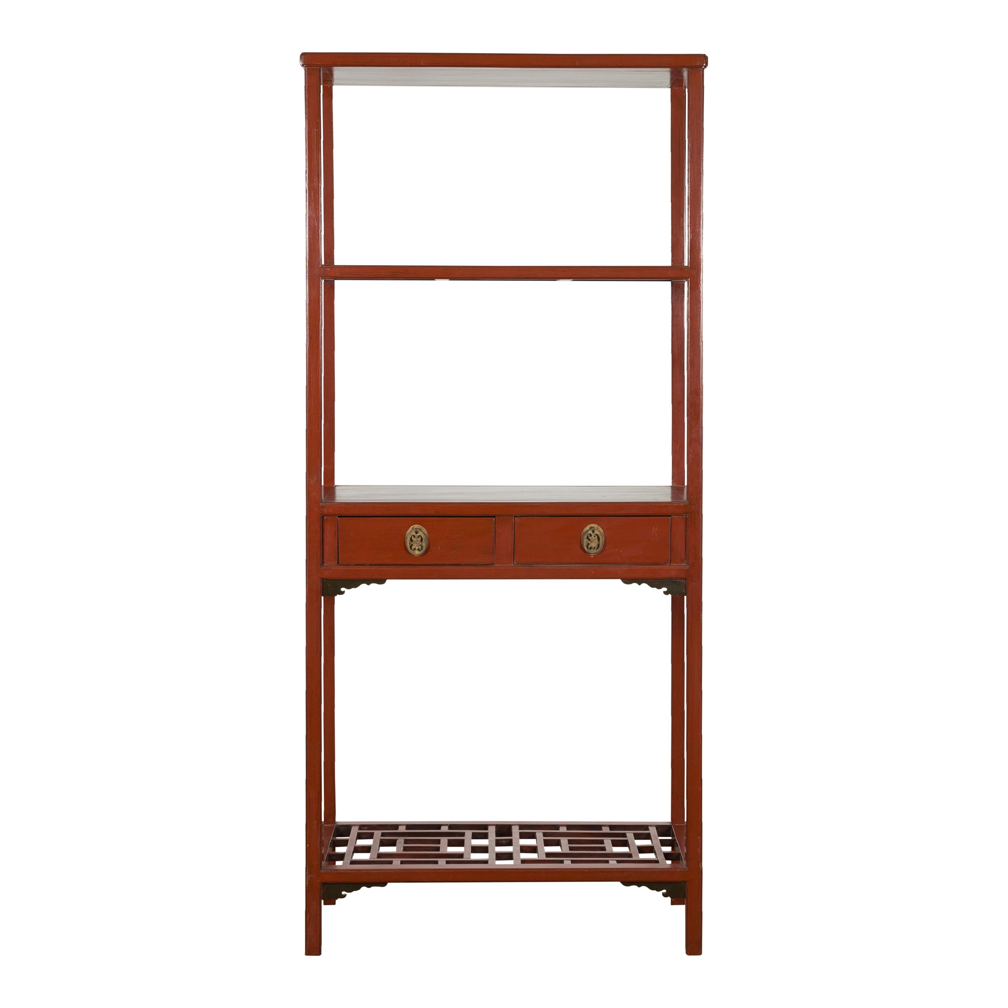 A Chinese late Qing Dynasty period red lacquer open bookshelf from the early 20th century, with two drawers, carved spandrels and geometric fretwork shelf. Created in China during the late Qing Dynasty period in the early years of the 20th century,