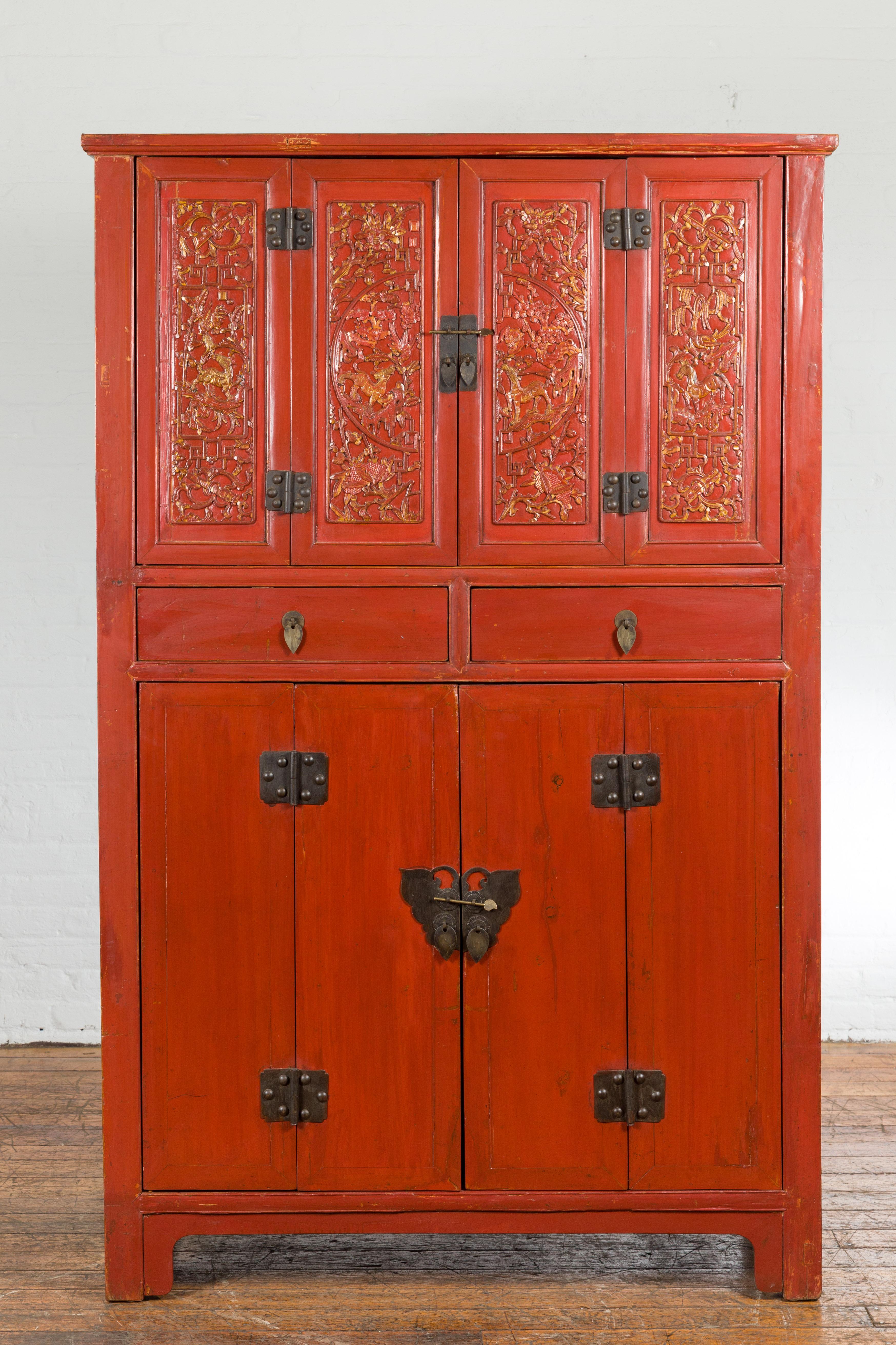 A Chinese late Qing Dynasty period red lacquered cabinet from the early 20th century, with butterfly hardware, two drawers, four doors, carved and gilt décor. Created in China during the late Qing Dynasty period in the early years of the 20th
