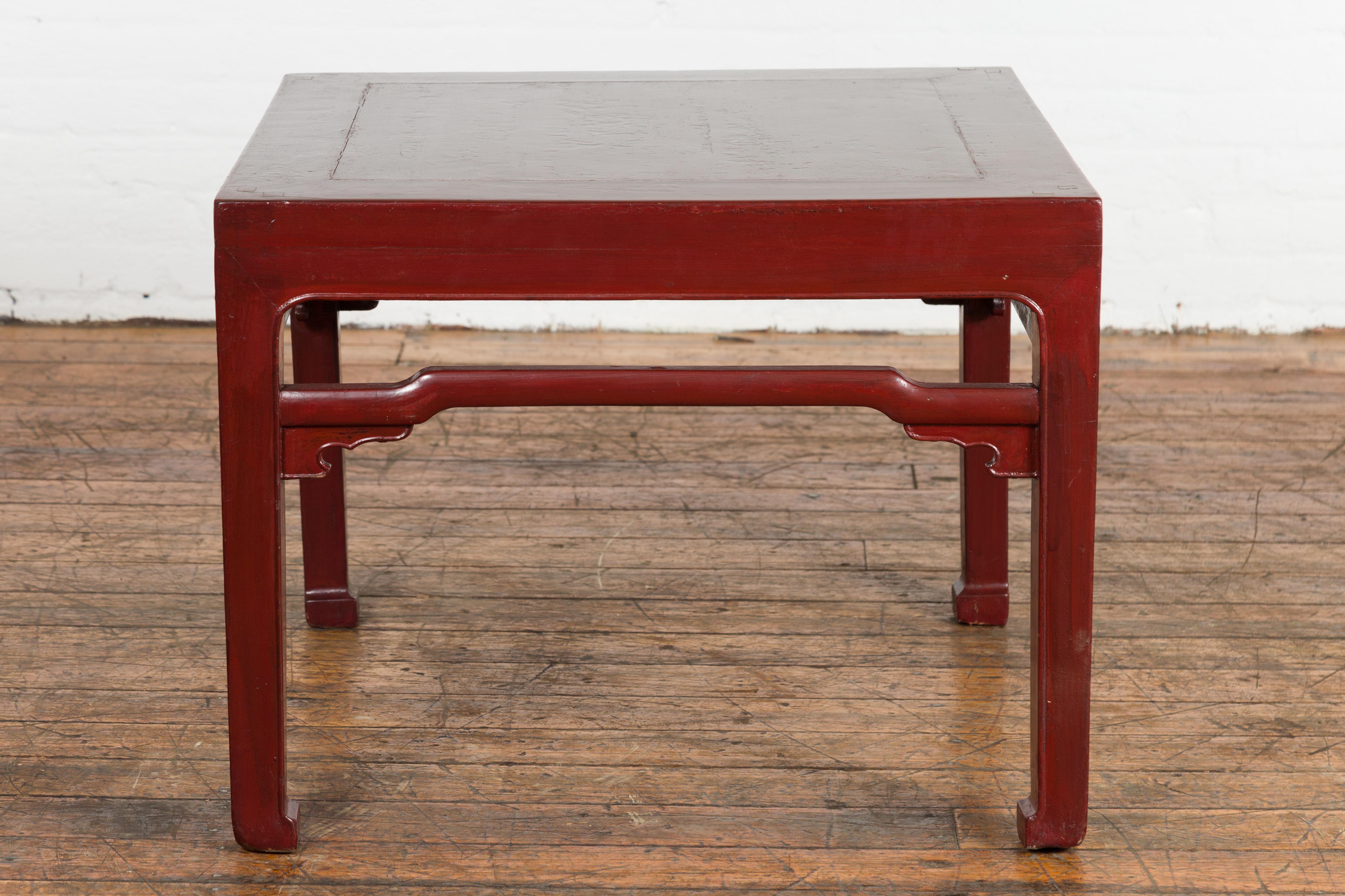 Chinese late Qing Dynasty period low table from the early 20th century, with red lacquer, horse hoof extremities, humpback stretchers and carved spandrels. This antique Qing Dynasty period low table radiates a warm, dark red lacquer. It is a