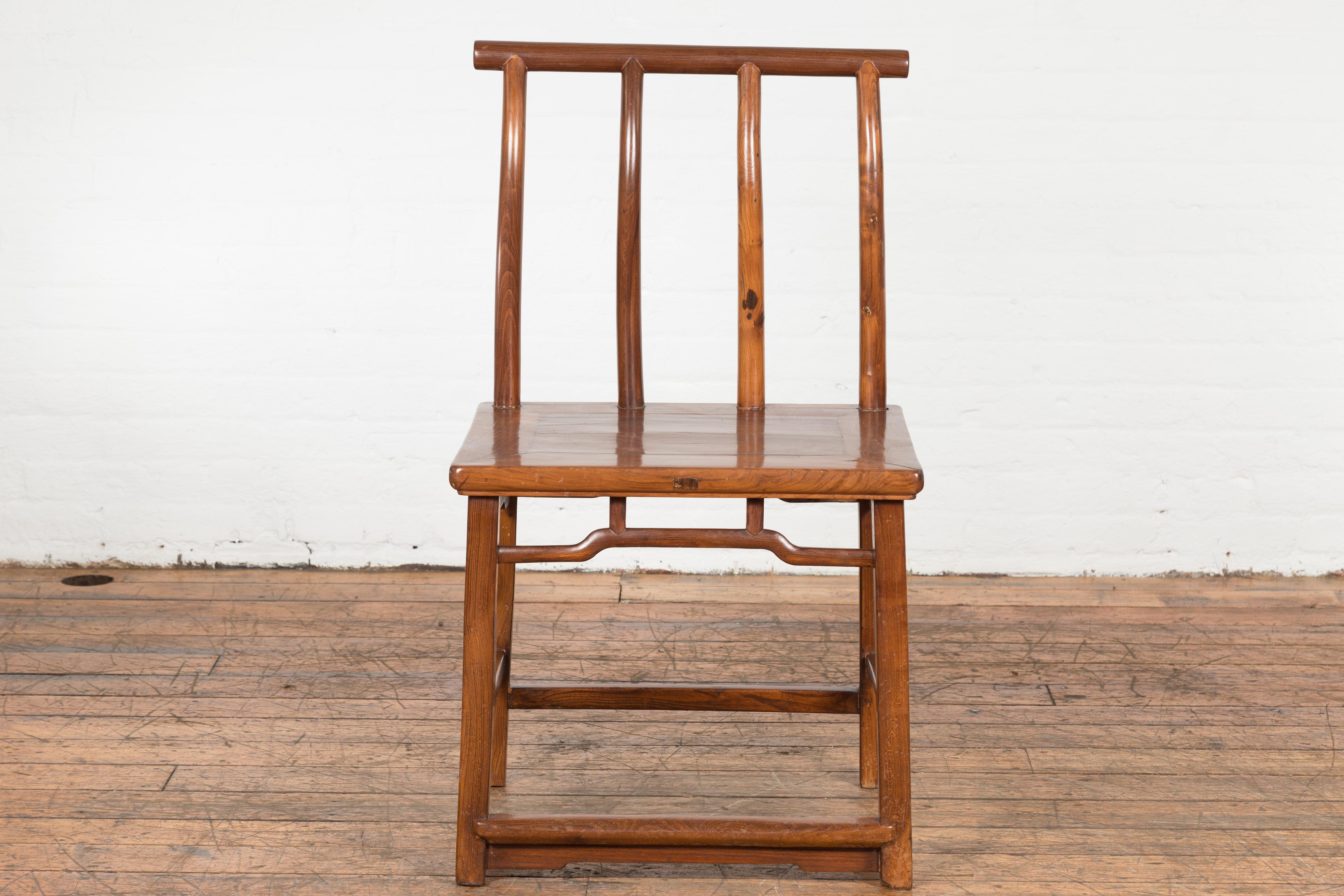 A Chinese late Qing Dynasty period chair from the early 20th century with vertical slats, pierced apron, pillar strut motifs and humpback stretchers. Exuding the richness of Chinese history, this early 20th century chair hails from the late Qing
