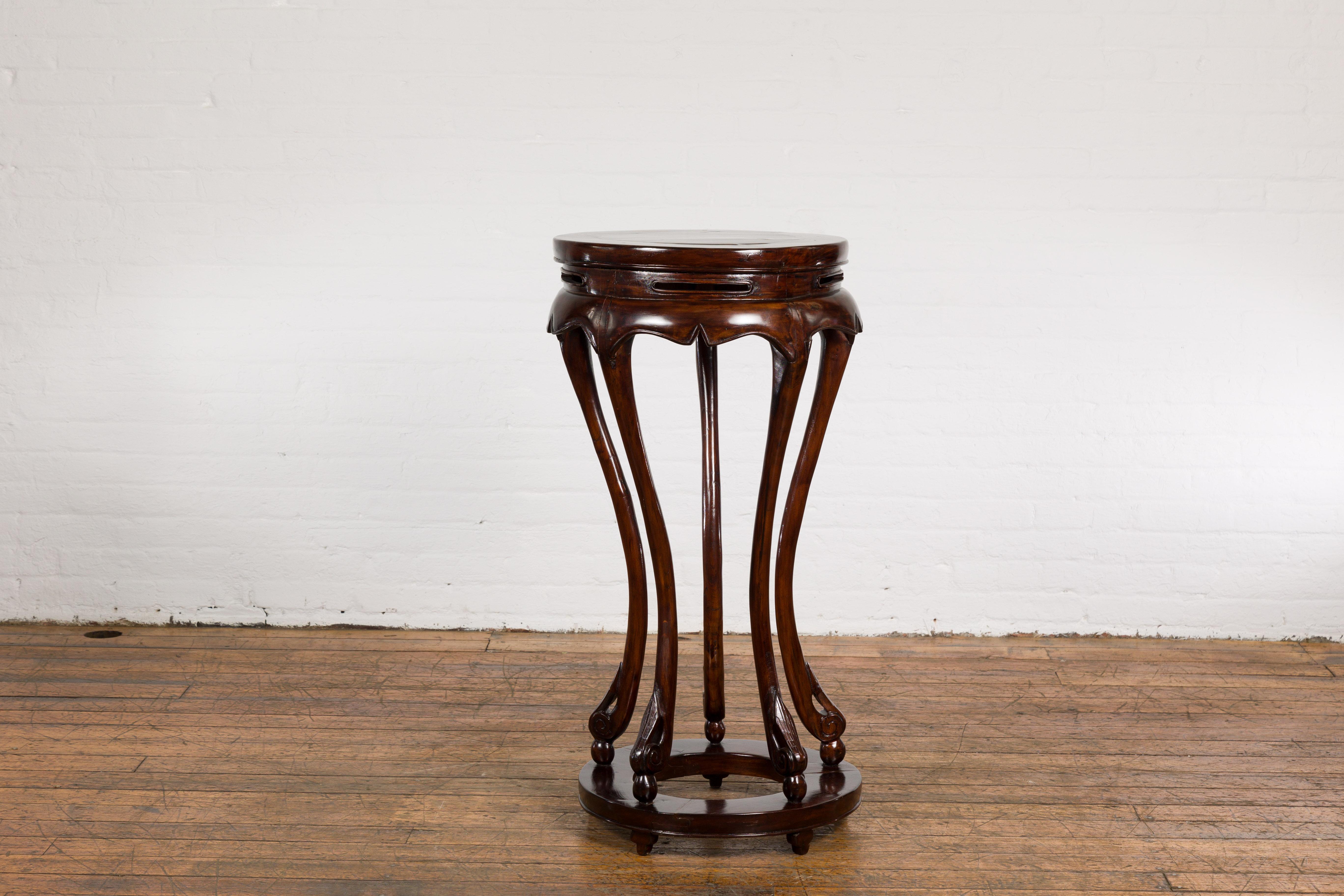 This Chinese late Qing Dynasty period wooden plant stand from the early 20th century features a circular top, carved apron, gracefully curving legs, low ring stretcher, and petite feet. This piece embodies the timeless allure and exceptional