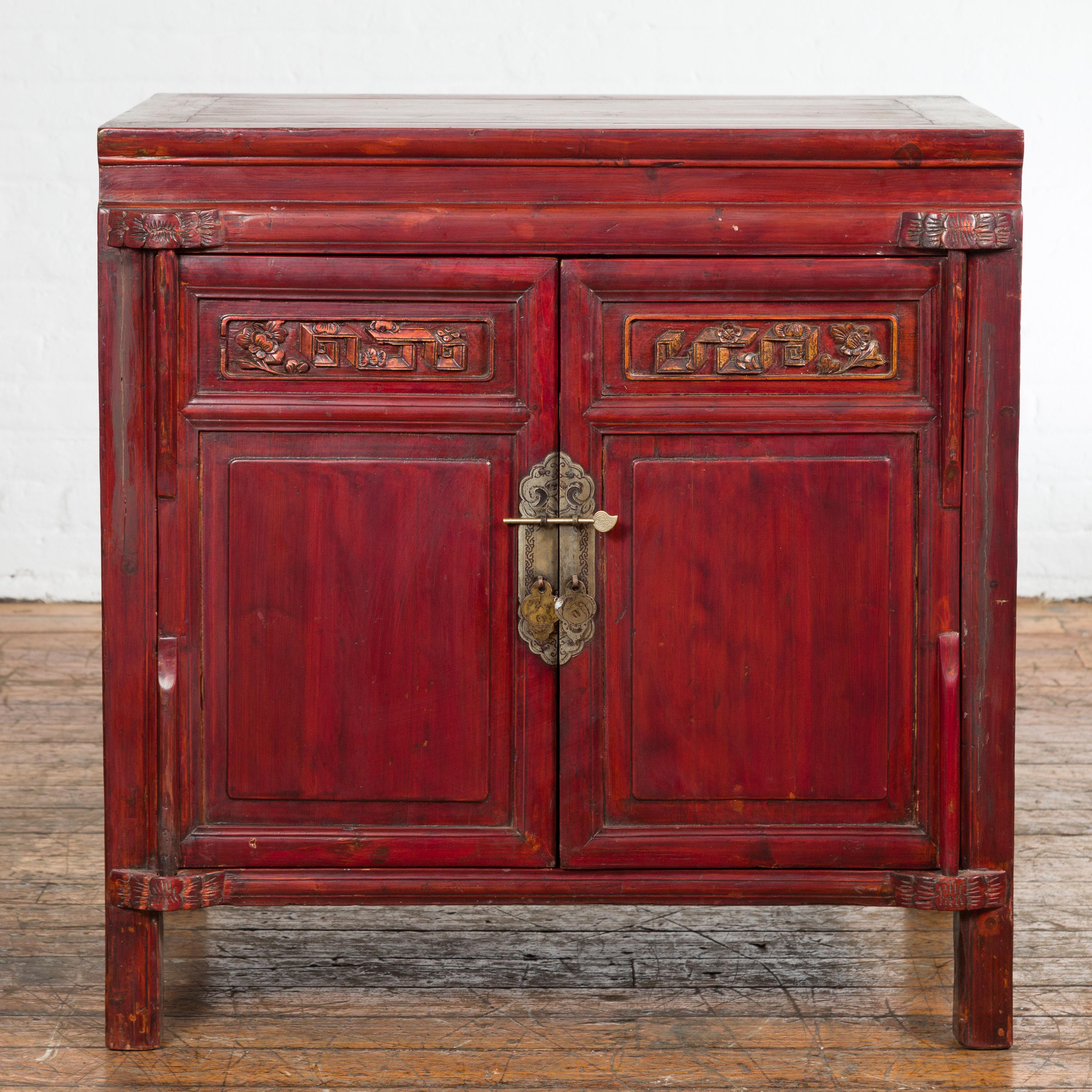A Chinese late Qing Dynasty period bedside cabinet from the early 20th century, with red lacquer, two doors, hidden drawers, carved décor and brass hardware. Created in China during the late Qing Dynasty period in the early years of the 20th