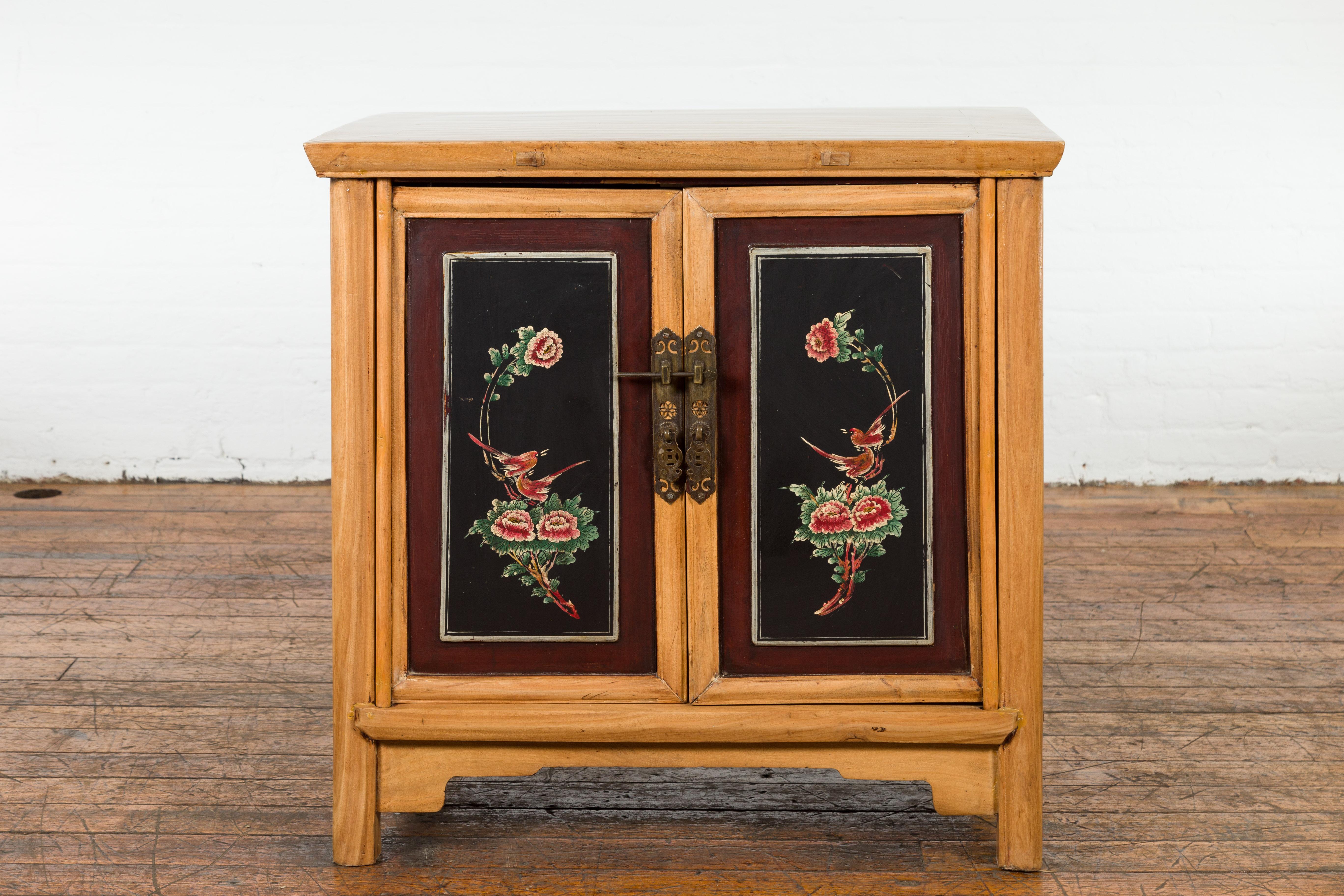 A Chinese late Qing Dynasty period side cabinet from the early 20th century, with hand painted flower and bird décor, two doors, ornate brass hardware, carved apron and custom lacquer. Created in China during the late Qing Dynasty period in the
