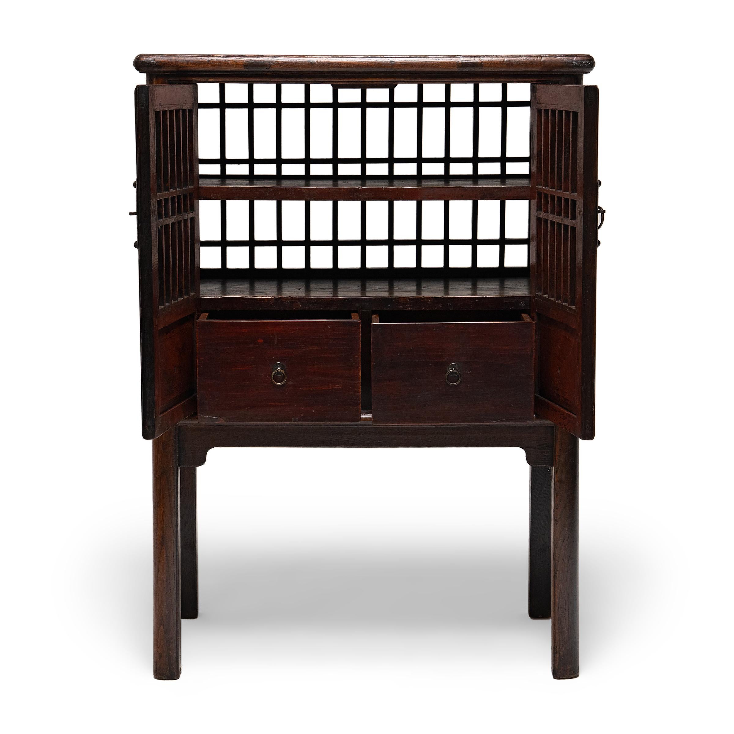 This 19th century kitchen cabinet is known as a catbox, named for its original use in keeping cats, dogs and other household pets away from food stored within. Petite in scale, the elevated chest has two shelves and two drawers enclosed by lattice