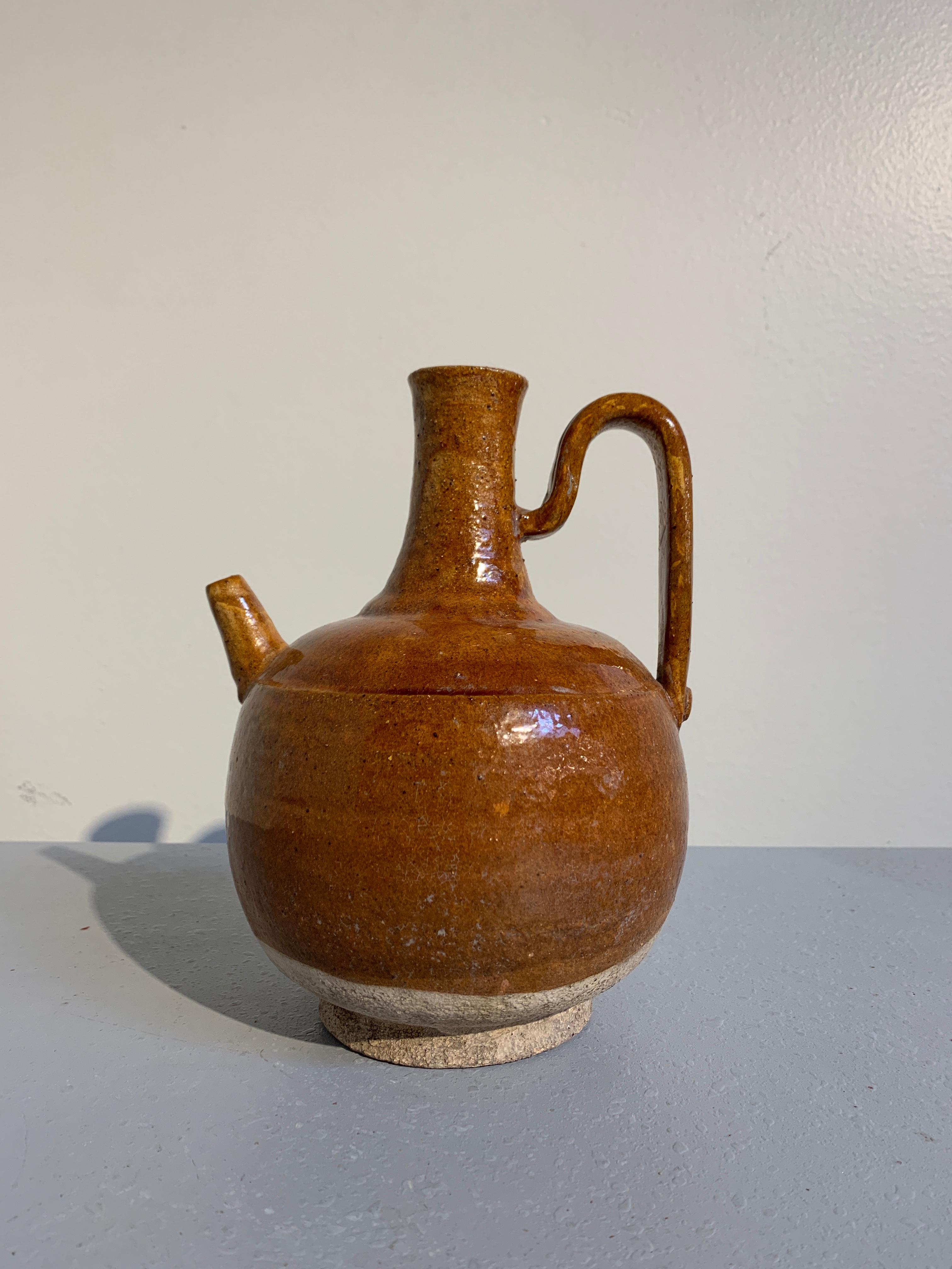 Joli récipient à bec verseur en poterie à glaçure ambrée, dynastie Liao (907 à 1125 ADS). 

Le récipient présente un corps globulaire avec un col allongé, une bouche légèrement évasée, un bec court et une poignée en forme de sangle. Les récipients