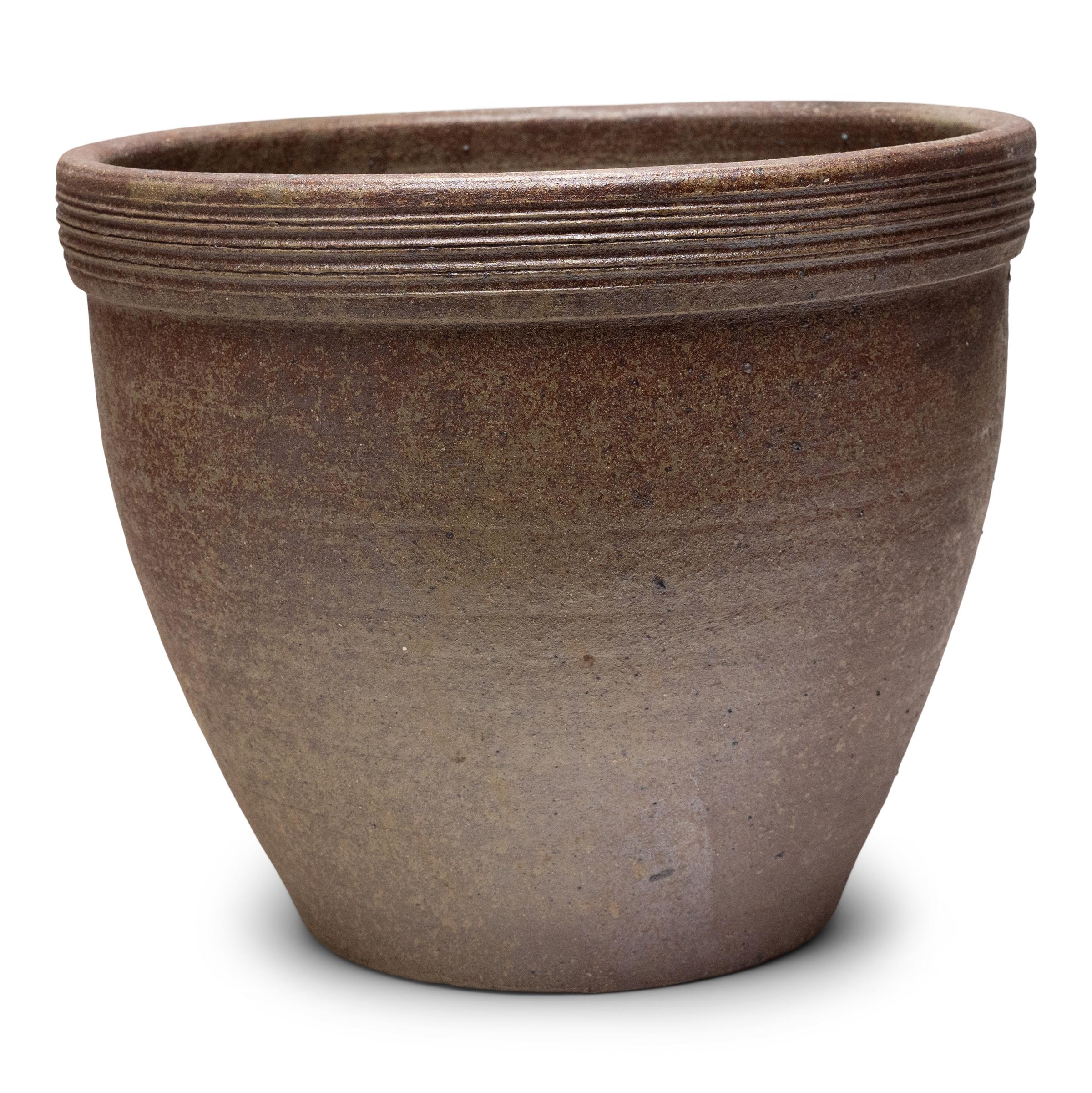 Ce petit bac à plantes en terre cuite est doté d'une forme minimale et d'une finition joliment irrégulière. Le récipient en céramique a une silhouette effilée, avec une large embouchure, une base rétrécie et un large bord orné de stries