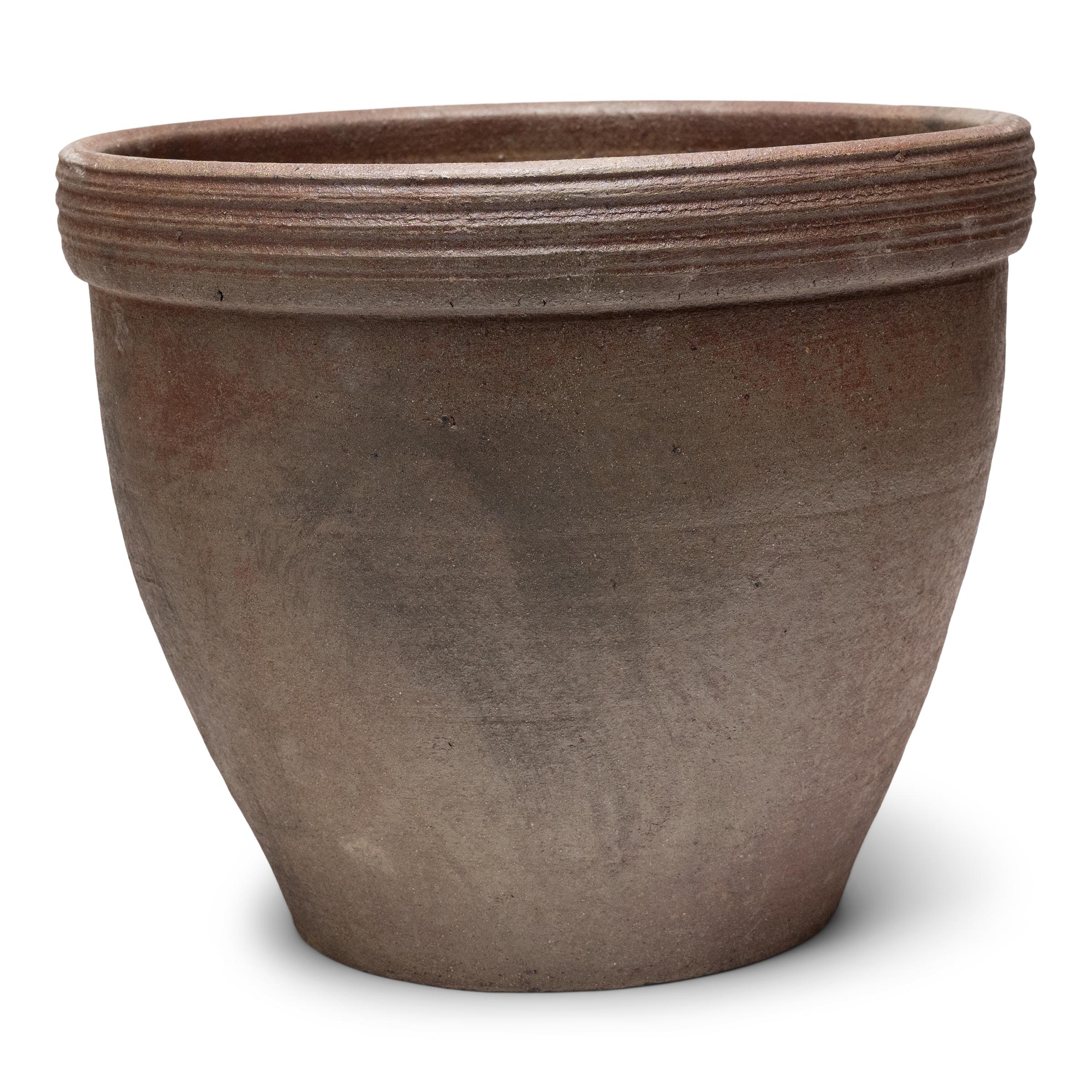 Ce petit bac à plantes en terre cuite est doté d'une forme minimale et d'une finition joliment irrégulière. Le récipient en céramique a une silhouette effilée, avec une large embouchure, une base rétrécie et un large bord orné de stries