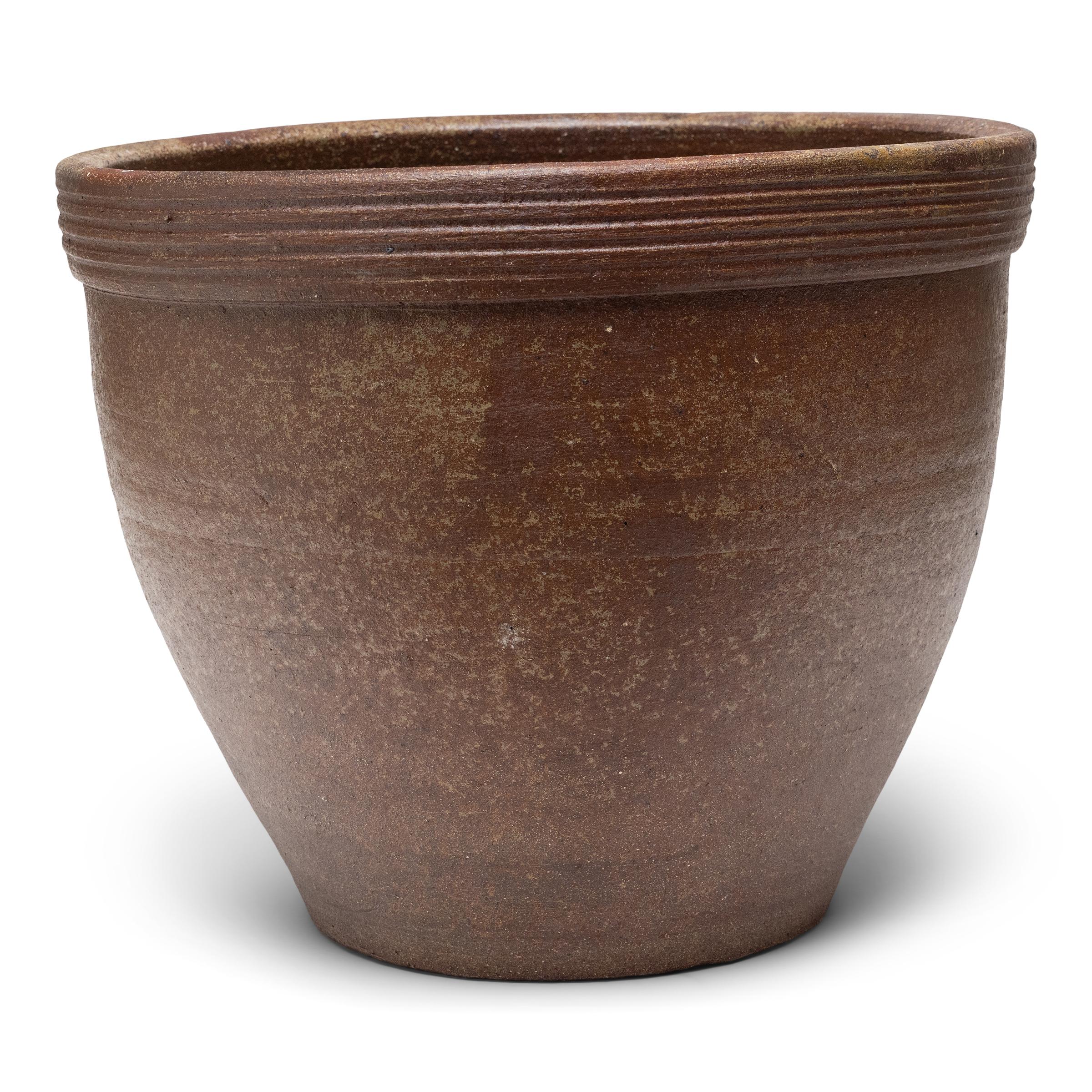 Ce petit bac à plantes en terre cuite est doté d'une forme minimale et d'une finition joliment irrégulière. Le récipient en céramique a une silhouette effilée, avec une large embouchure, une base rétrécie et un large bord orné de stries