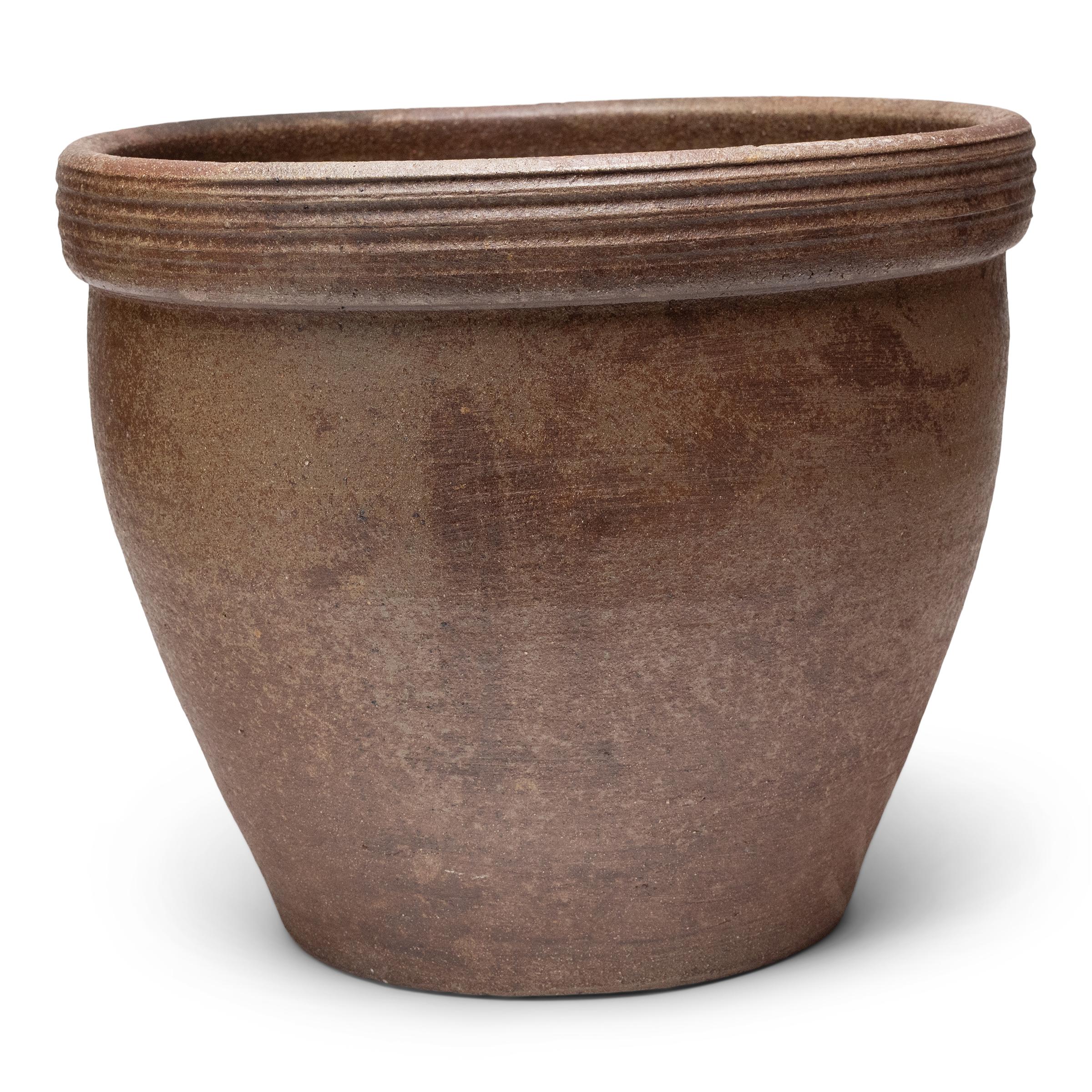 Ce petit bac à plantes en terre cuite est doté d'une forme minimale et d'une finition joliment irrégulière. Le récipient en céramique a une silhouette effilée, avec une large embouchure, une base rétrécie et un large bord orné de stries