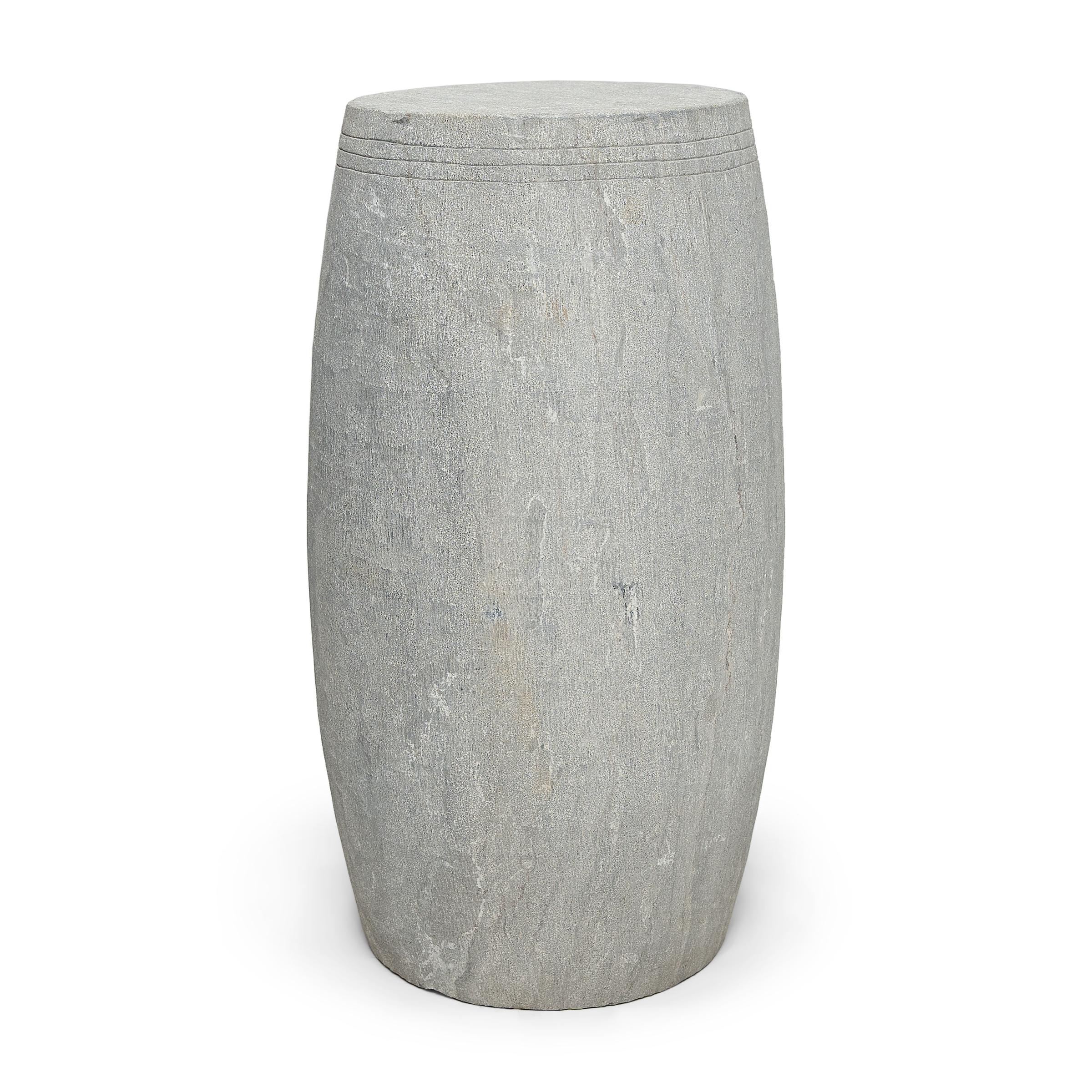 This narrow drum stool was carved from a solid block of limestone with a minimalist tapered design. The stool is subtly etched with thin grooves around the top, suggestive of the lines drawn by stretched hide on an actual drum. Traditionally used as