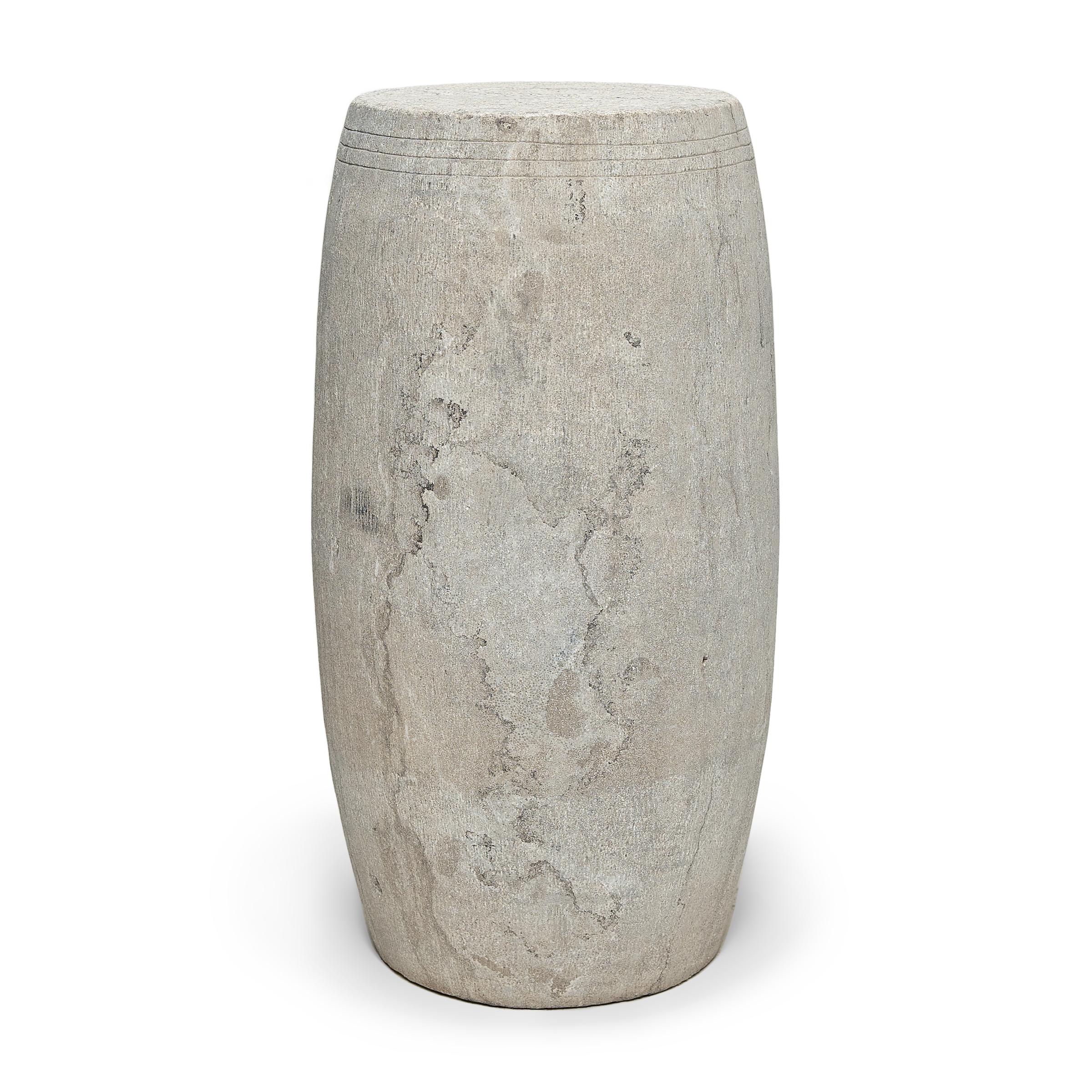 This narrow drum stool was carved from a solid block of limestone with a Minimalist tapered design. The stool is subtly etched with thin grooves around the top, suggestive of the lines drawn by stretched hide on an actual drum. Traditionally used as